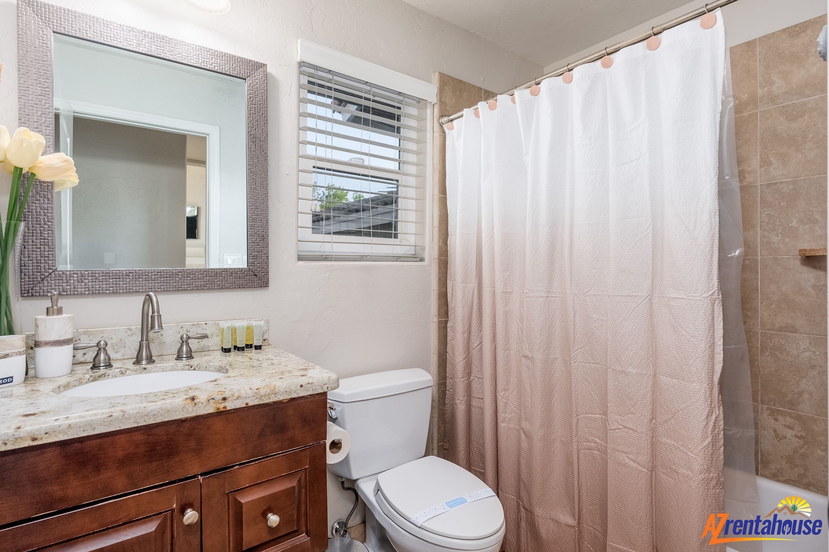 Freshen up in your private bathroom with granite countertops, warm wood cabinetry, and a tiled shower with a calming rose-tinted curtain. Soft light and elegant touches make mornings feel effortless.