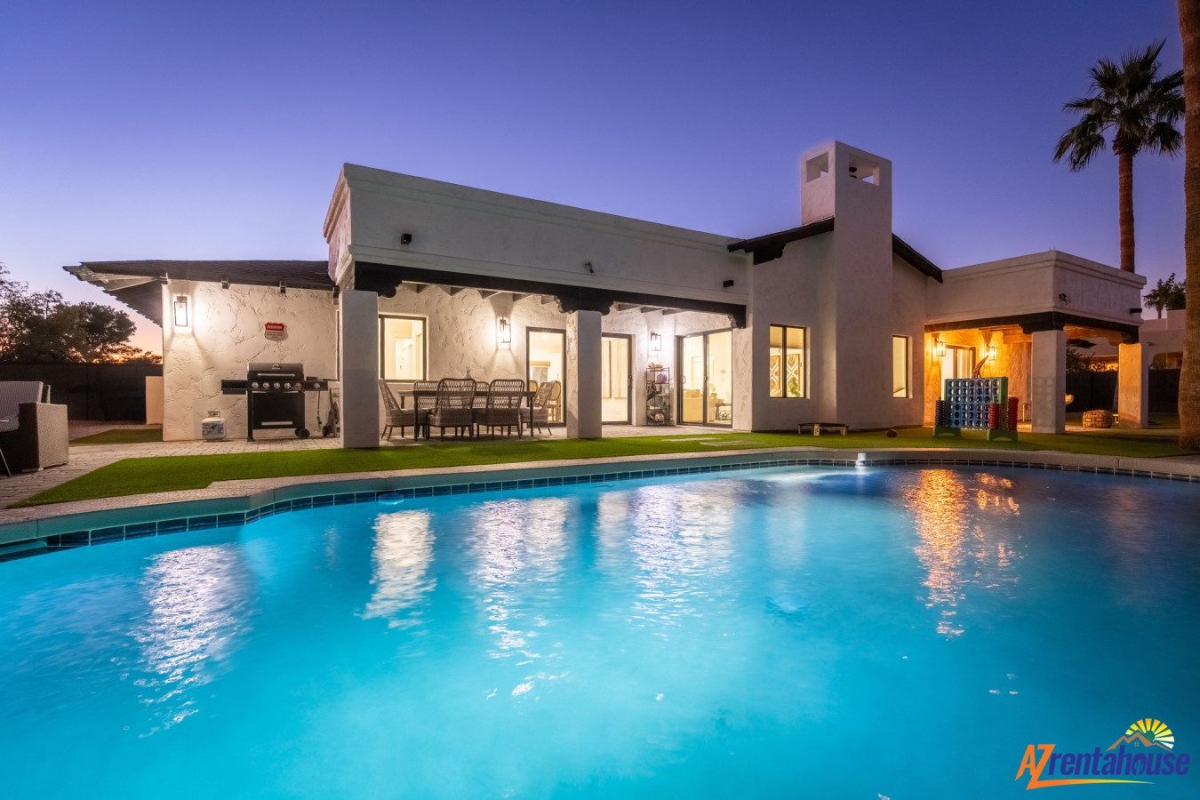 Modern desert retreat with sparkling pool and BBQ area set against twilight skies and swaying palms.