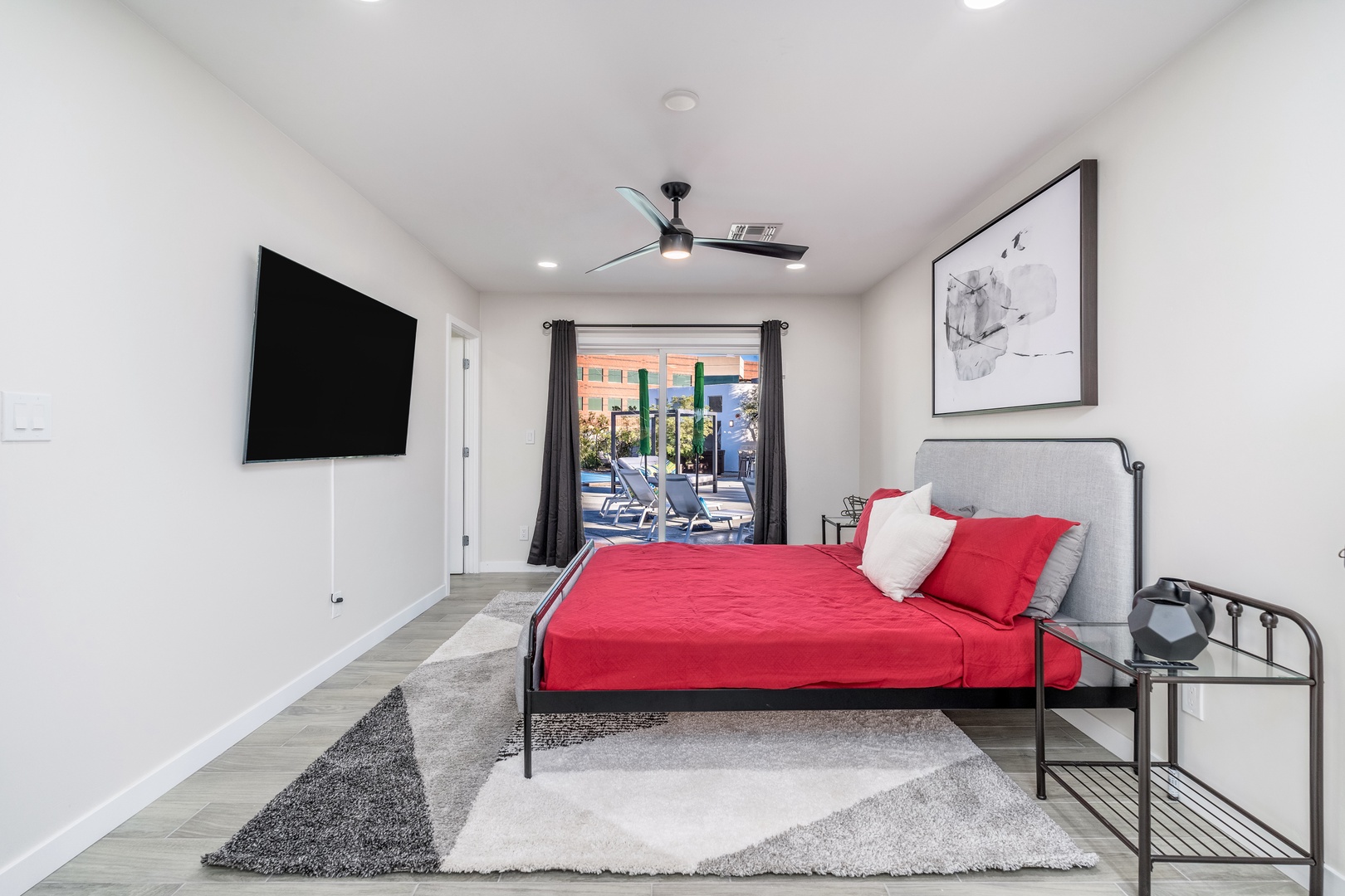 Your bright, modern retreat features a plush bed with bold red linens, a wall-mounted TV for cozy evenings, and poolside doors that invite you to step outside and unwind in the sunshine.