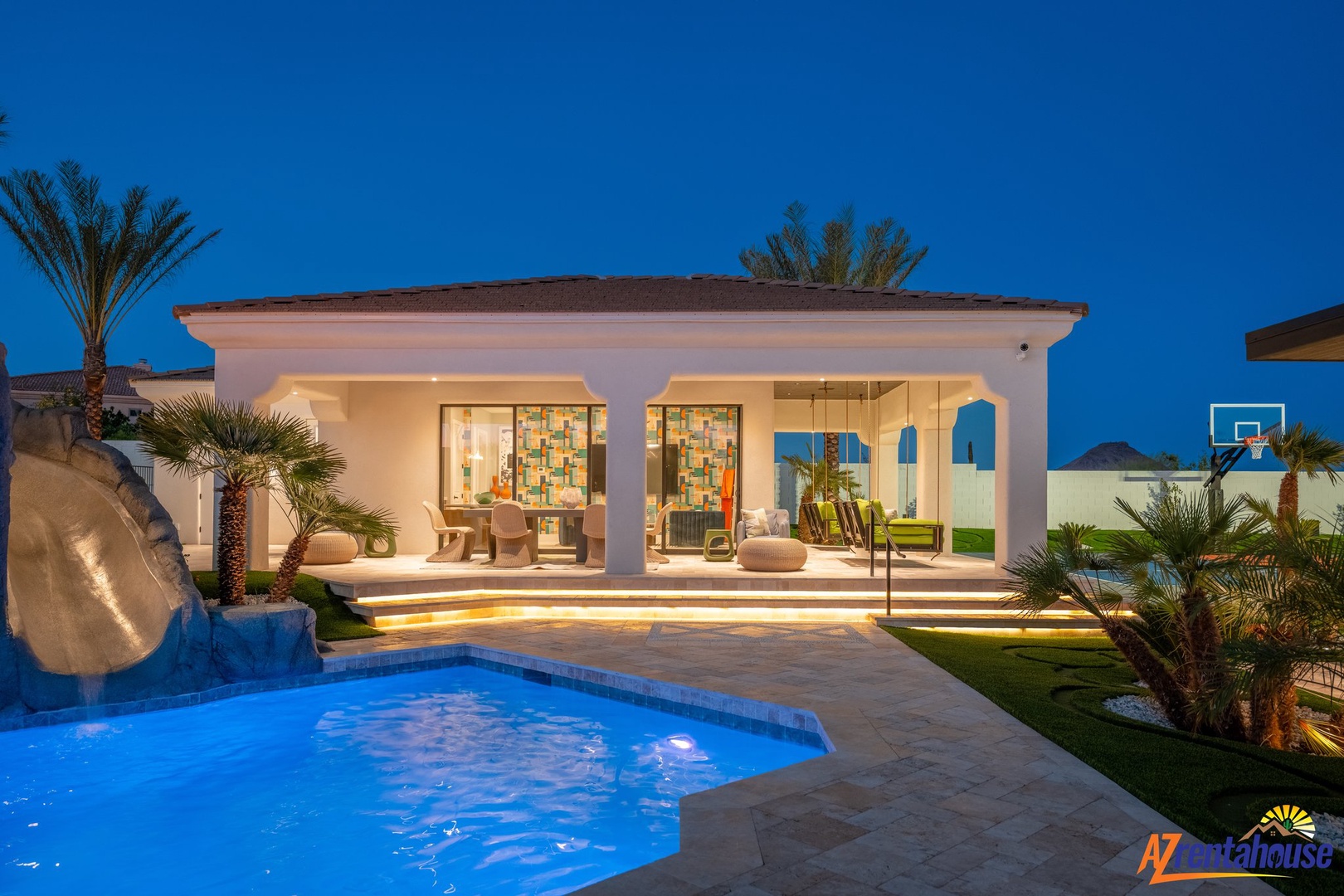 Modern villa features an illuminated swimming pool and spacious outdoor terrace surrounded by tropical palms under evening sky.