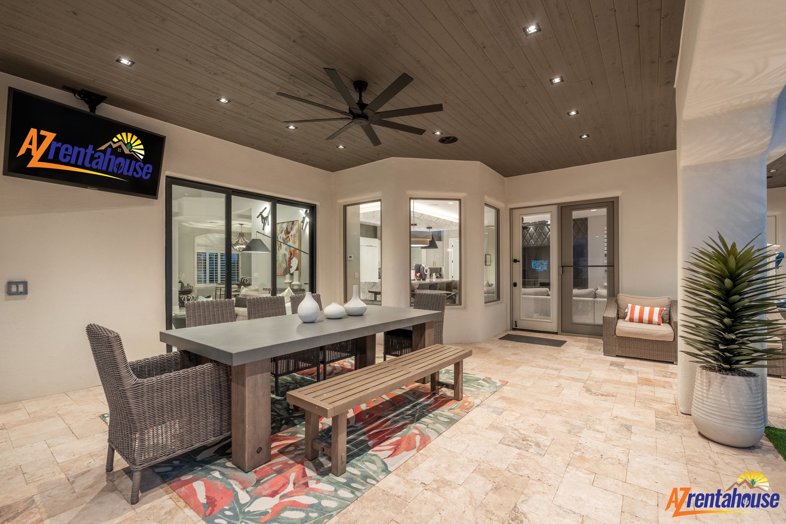 Your covered patio features modern dining for eight with wicker seating, colorful rug, and ceiling fan for perfect outdoor entertaining.