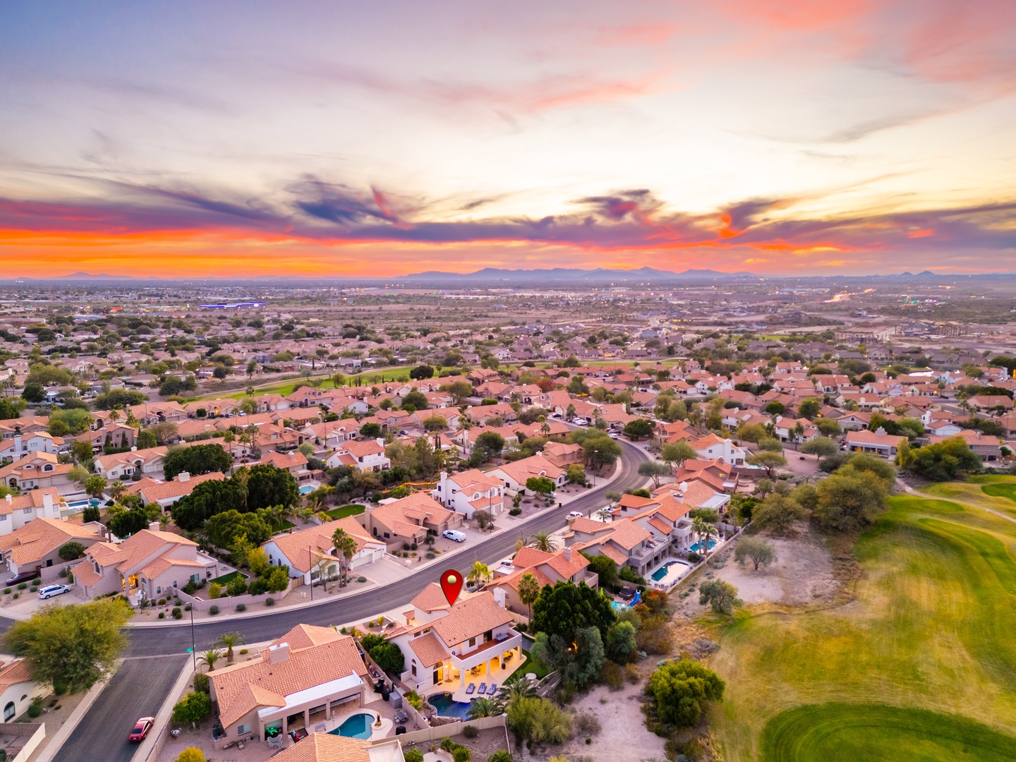 Aerial view of a residential neighborhood at sunset, showcasing the property's location within a peaceful community near a golf course and mountain vistas.