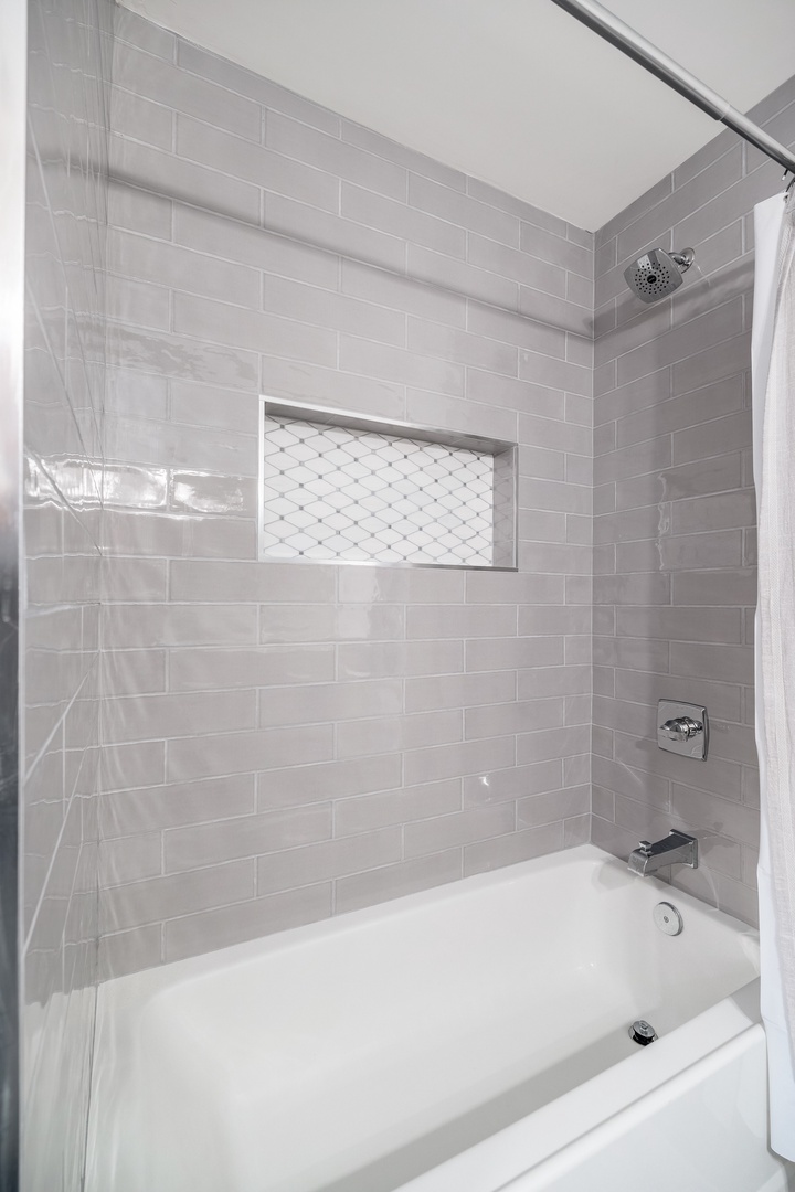 Soak away your day in this pristine tub-shower combo. Soft gray subway tiles and a rainfall showerhead create your own serene retreat.