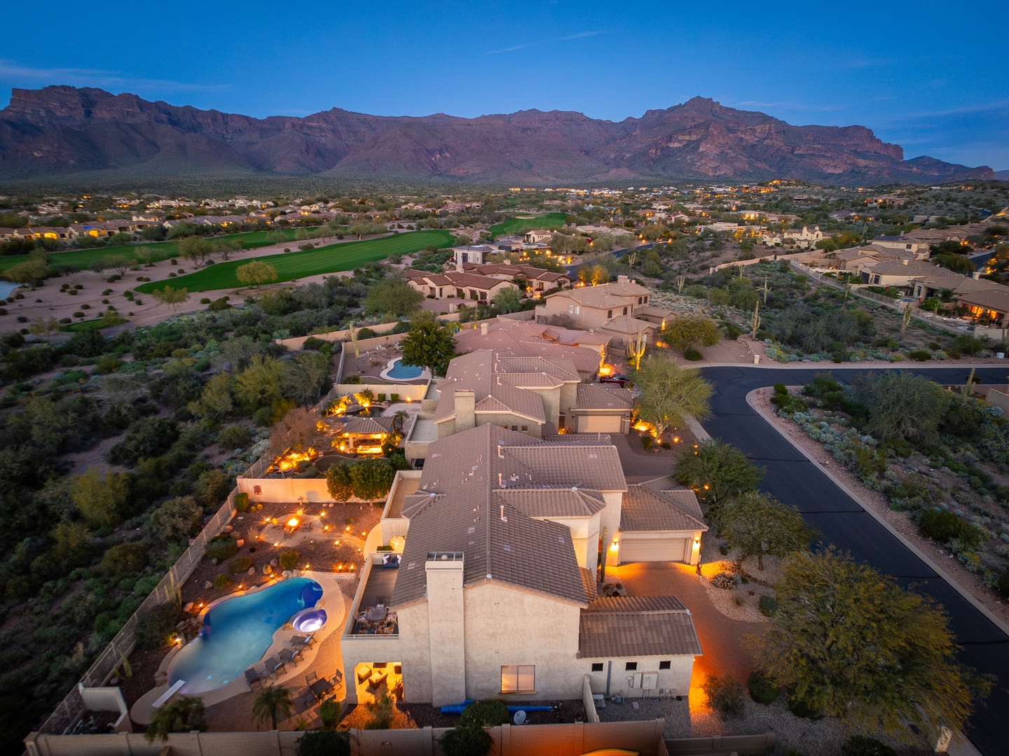 Aerial view of a desert luxury estate at dusk, showcasing southwestern architecture, private pools, manicured grounds, and dramatic mountain backdrop in the surrounding landscape.