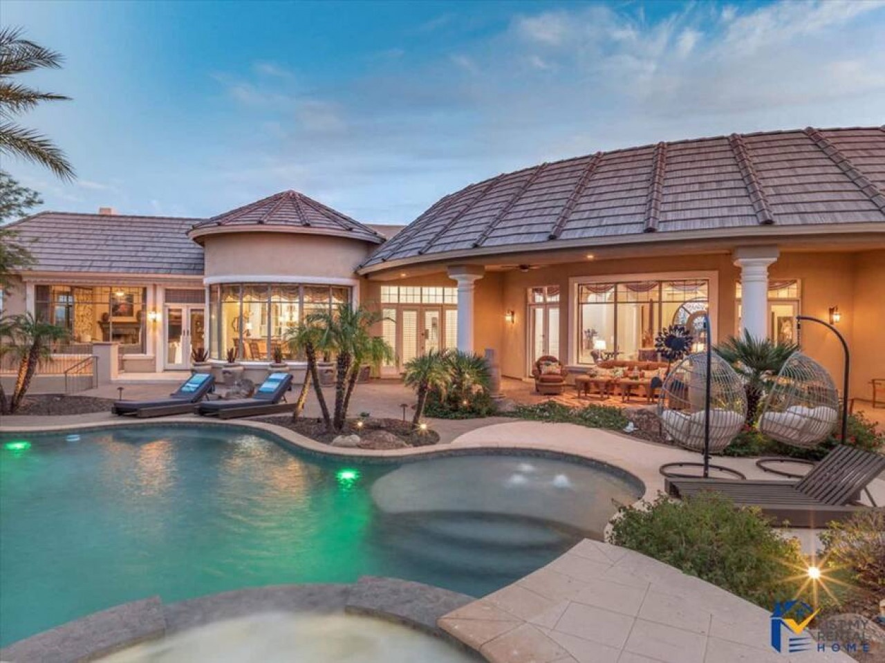 Luxury villa exterior featuring swimming pool with spa, tropical landscaping, and elegant outdoor seating areas at twilight.