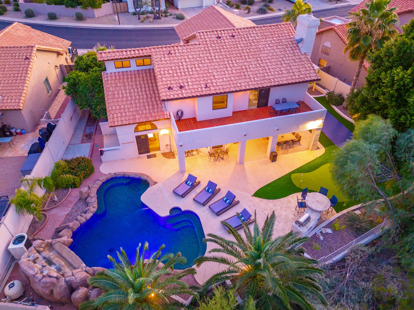 Aerial view of a vacation rental featuring a custom pool with rock waterfall, spacious covered patio with dining area, and landscaped backyard in a quiet residential neighborhood.