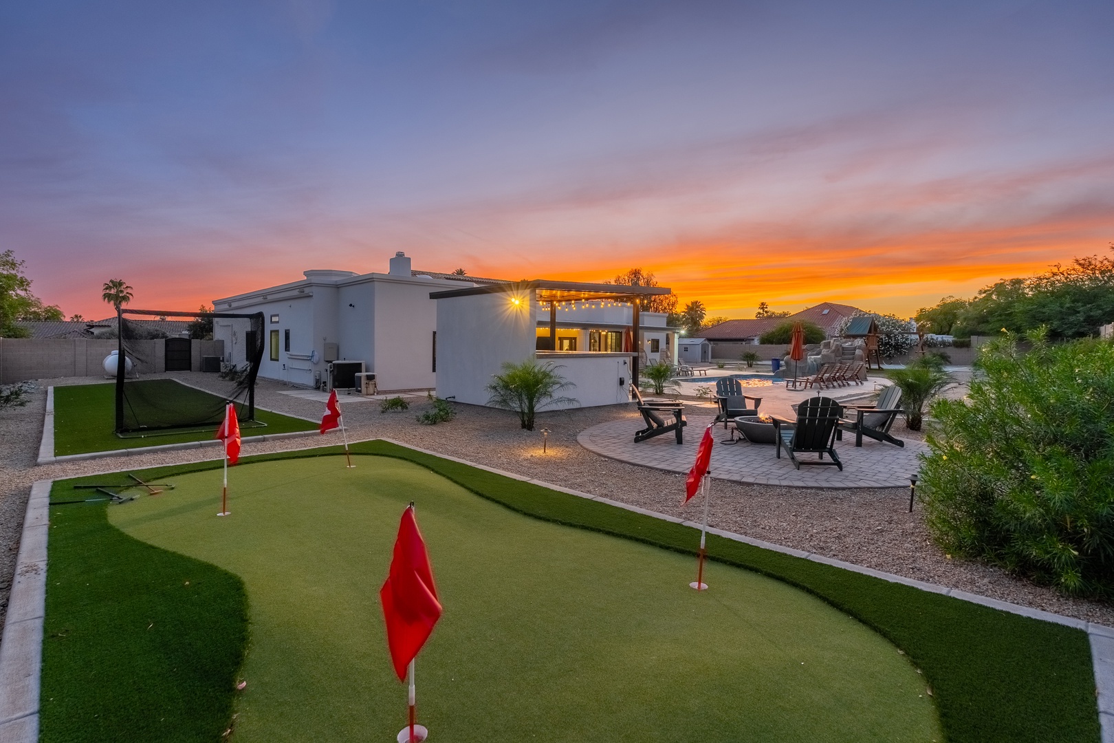 A stunning desert property featuring a private putting green, heated pool, fire pit seating area, and covered outdoor dining space beneath a brilliant Arizona sunset.