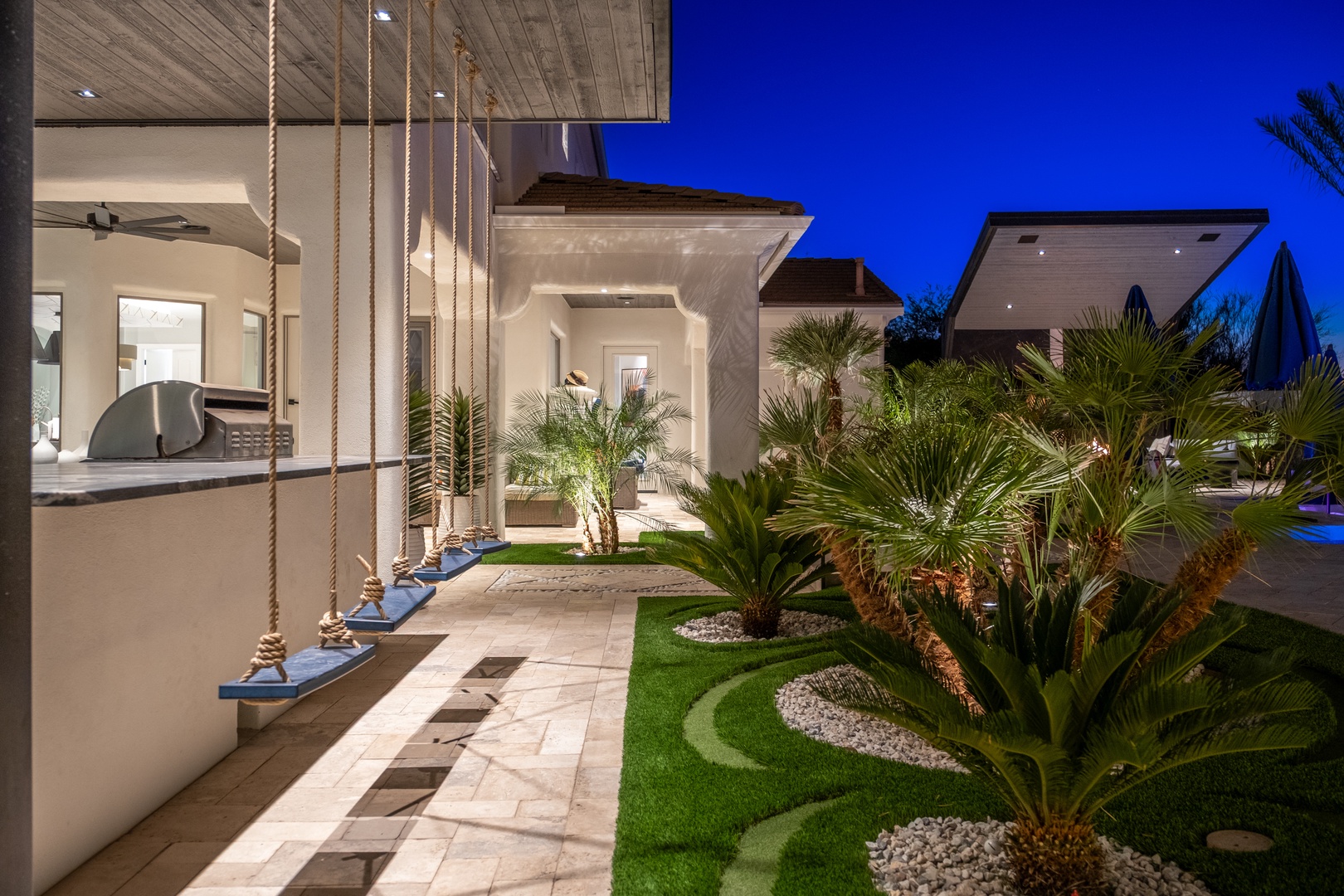Stunning contemporary architecture meets tropical landscaping at this luxurious property entrance, illuminated under the evening sky with palm-dotted gardens and sophisticated outdoor spaces.