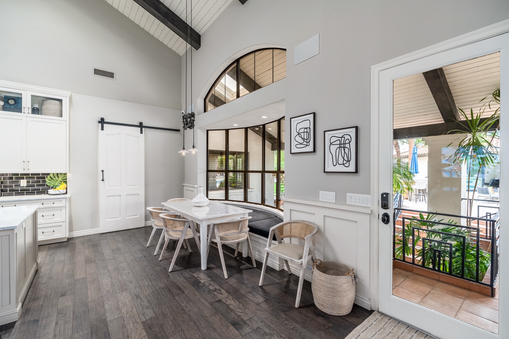 Gather around the farmhouse-style dining table under soaring vaulted ceilings, where natural light pours in from the loft above. The open barn door and patio access invite easy indoor-outdoor living.