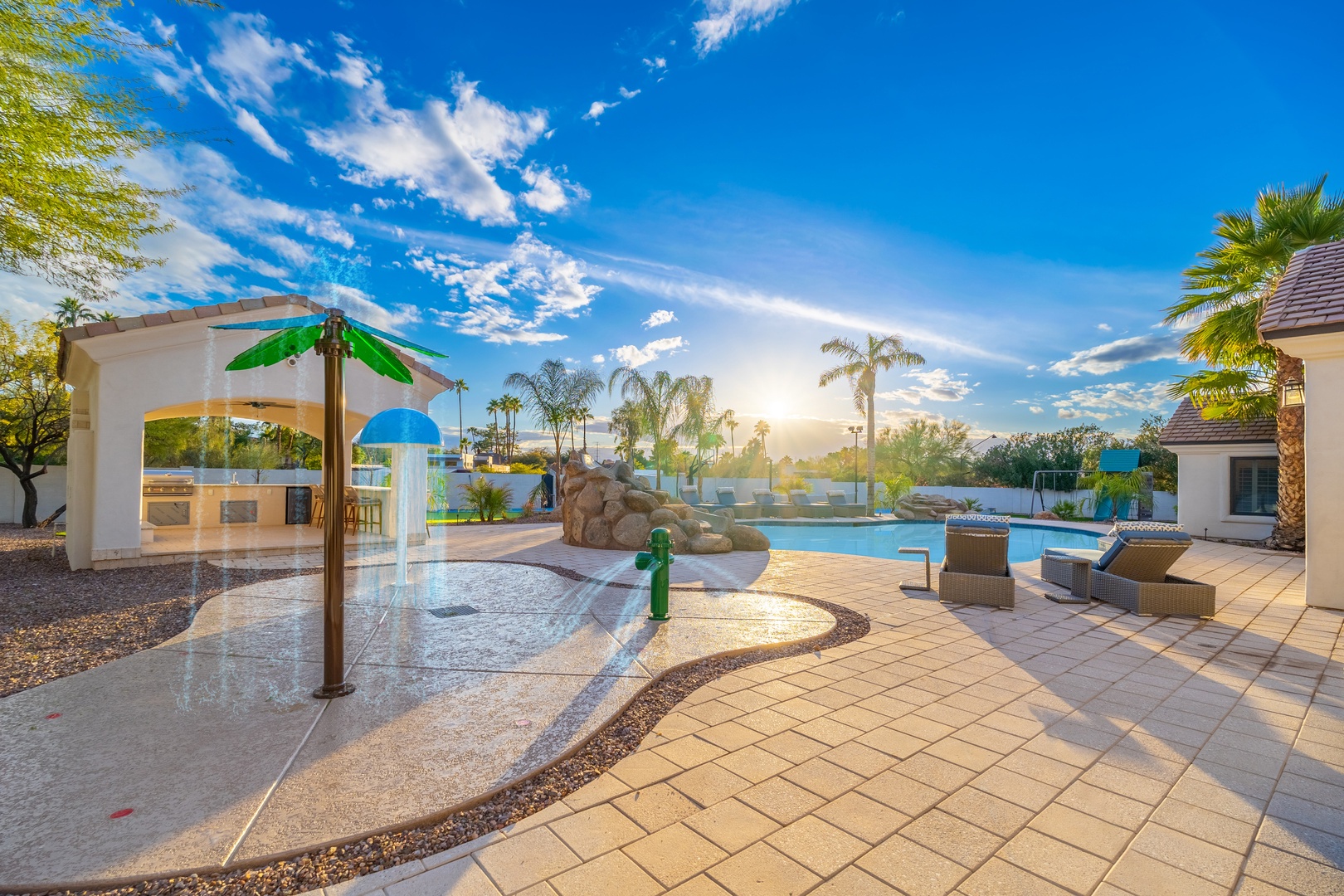 Your private resort oasis awaits with a splash pad, sparkling pool, and sunbathing loungers under swaying palms and endless blue skies.