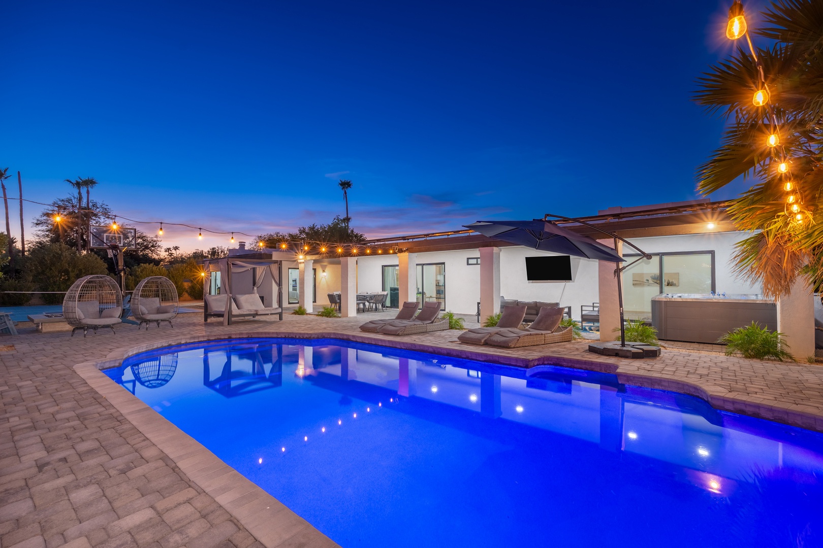 Stunning desert oasis with private pool illuminated under twilight skies. Modern architecture, ambient string lights, and spacious outdoor entertaining area create an inviting retreat for relaxation.
