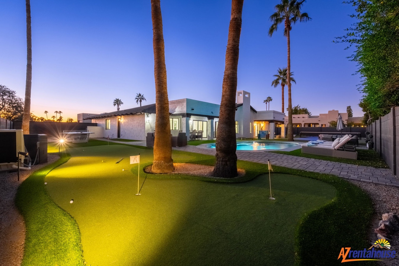 Luxurious desert vacation rental with private putting green, sparkling pool, and towering palm trees under twilight skies.