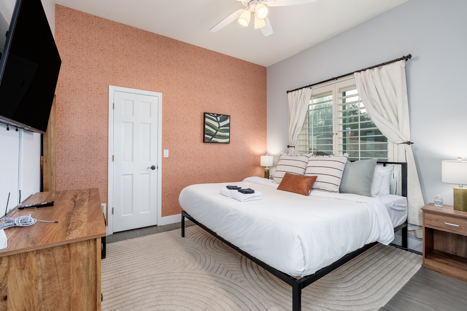 Unwind in your cozy bedroom with a plush bed, warm coral accent wall, and soft natural light streaming through plantation shutters. Your peaceful retreat awaits.