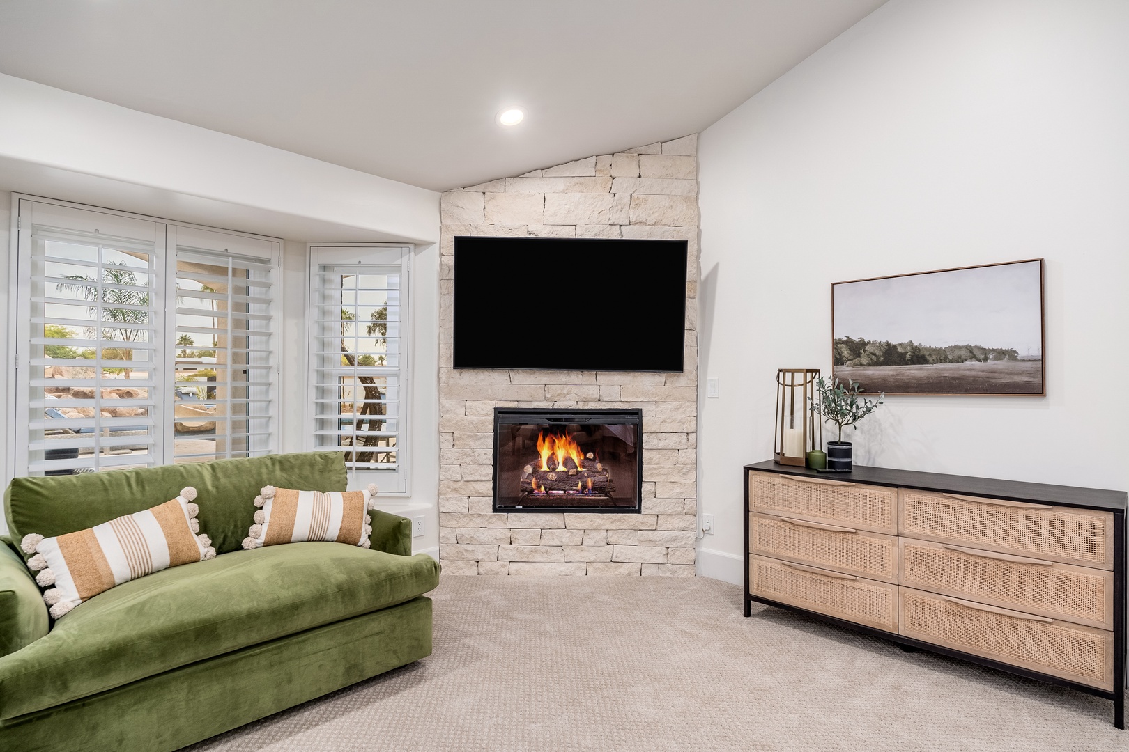 Curl up on the plush green sofa as flames dance in the stone fireplace, creating your perfect cozy evening retreat with views through plantation shutters.