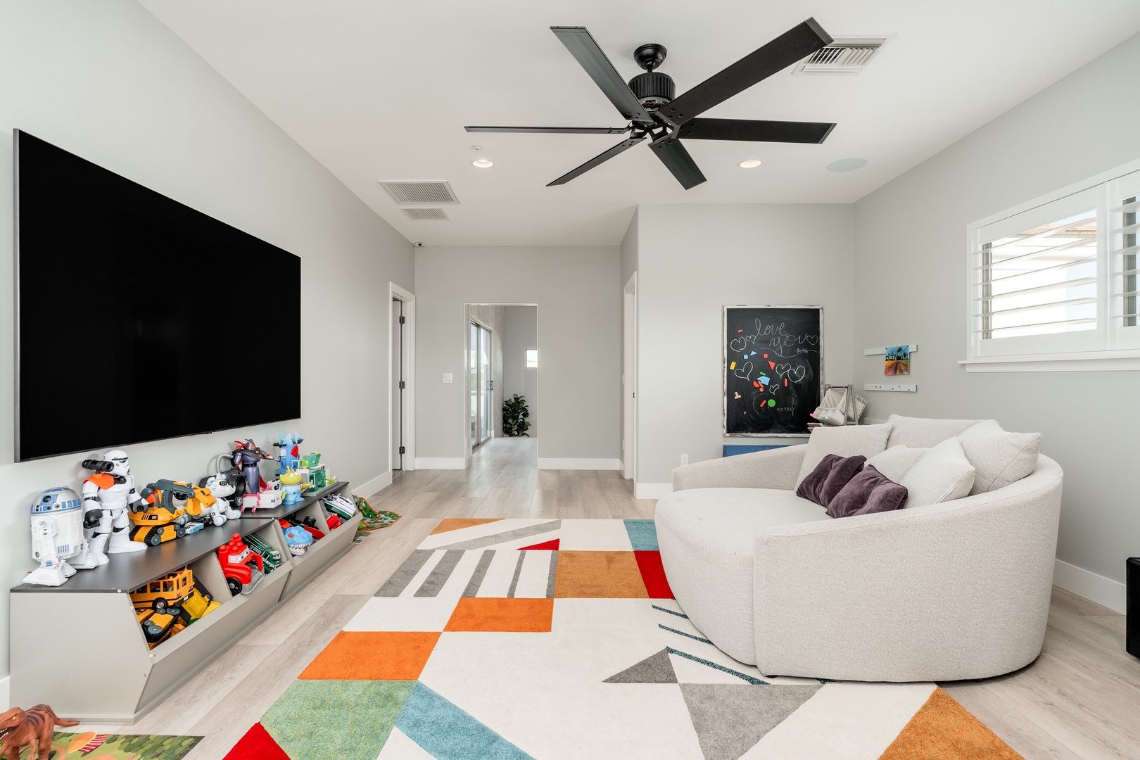 Unwind in your bright, modern living room with a cozy curved sofa, large flatscreen TV, and colorful rug—perfect for family movie nights or relaxing after a day exploring.