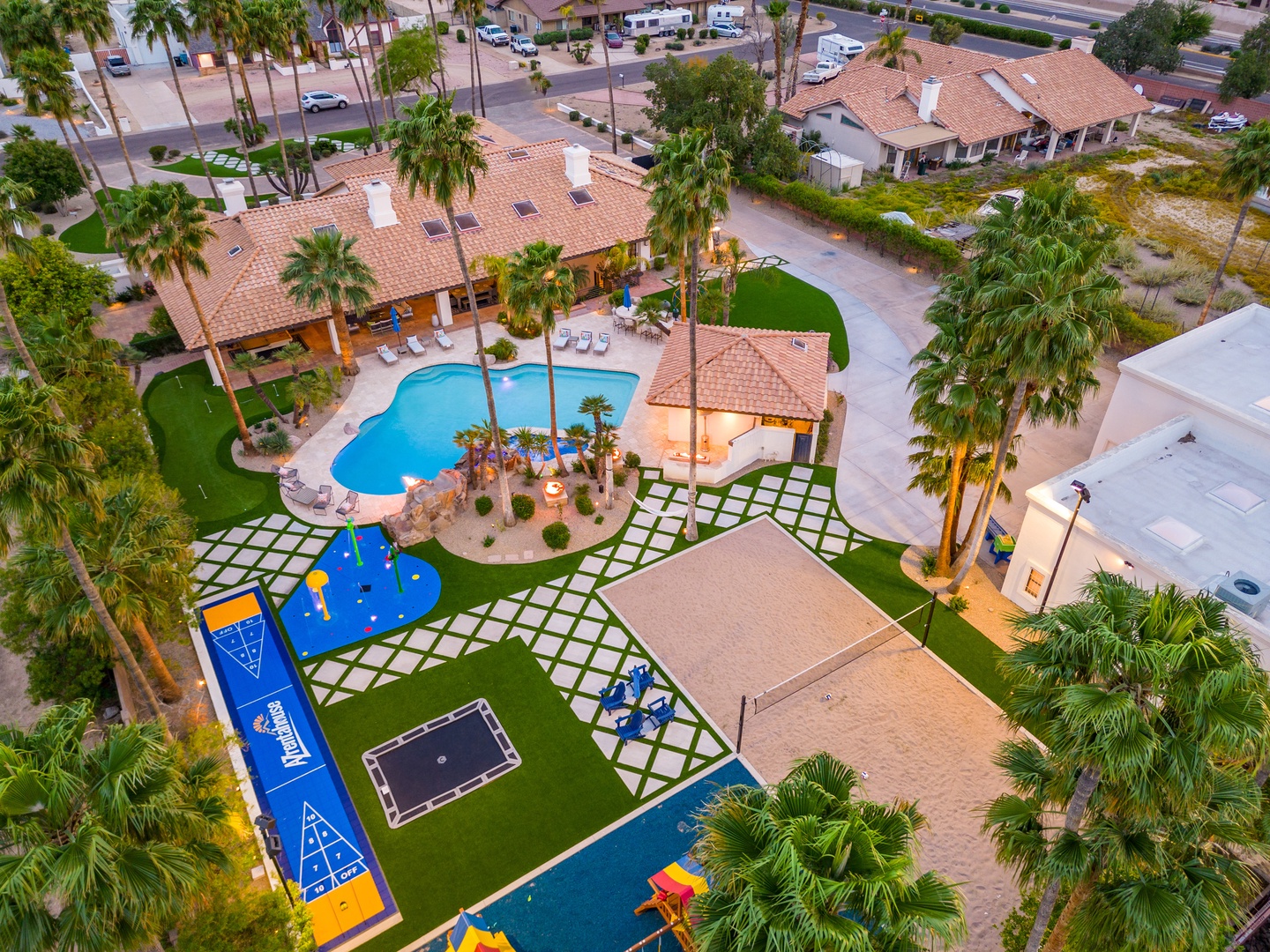 Aerial view of a luxury vacation property featuring a resort-style pool, miniature golf course, shuffleboard, and children's play area amid manicured tropical landscaping.