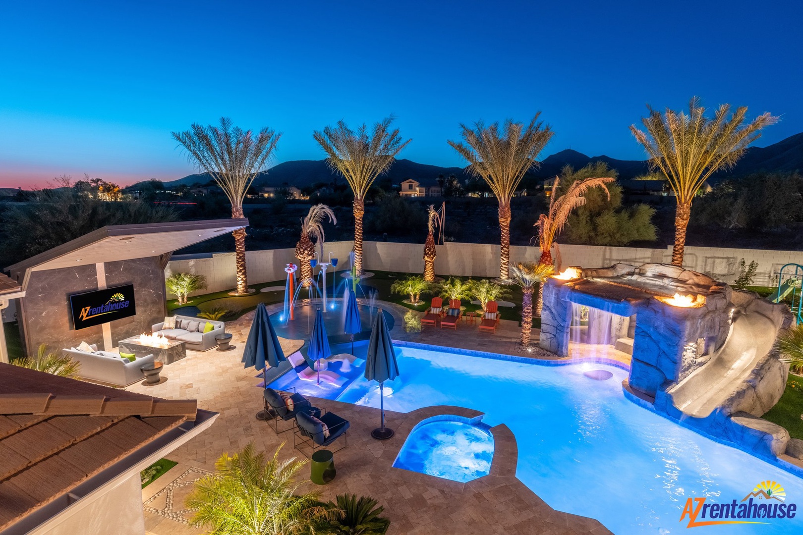 Stunning resort-style backyard featuring illuminated pool, spa, waterfall, and palm trees at twilight