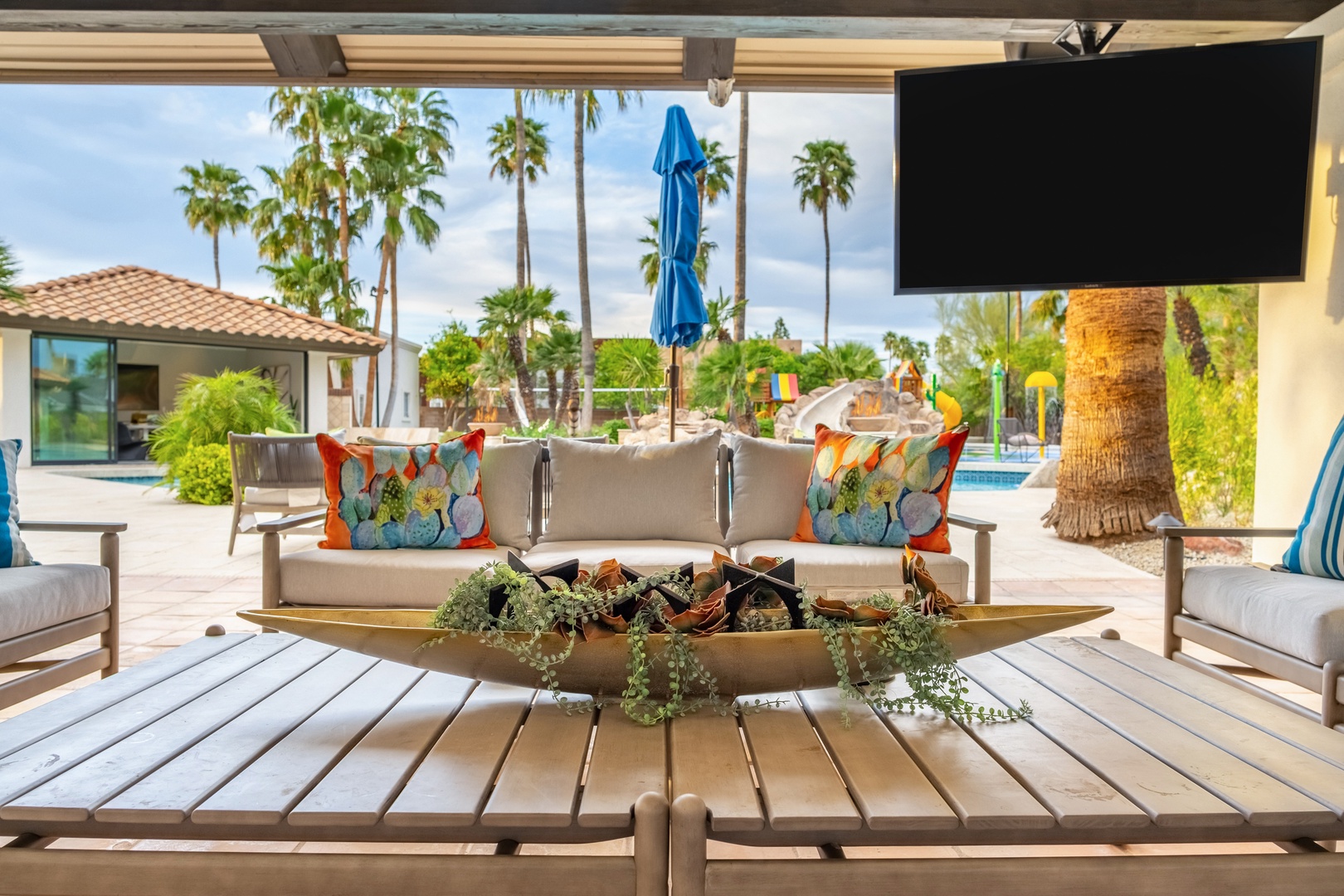 Your covered patio features plush seating and a flat-screen TV, perfect for lounging while enjoying views of swaying palms, the sparkling pool, and warm desert sunshine.