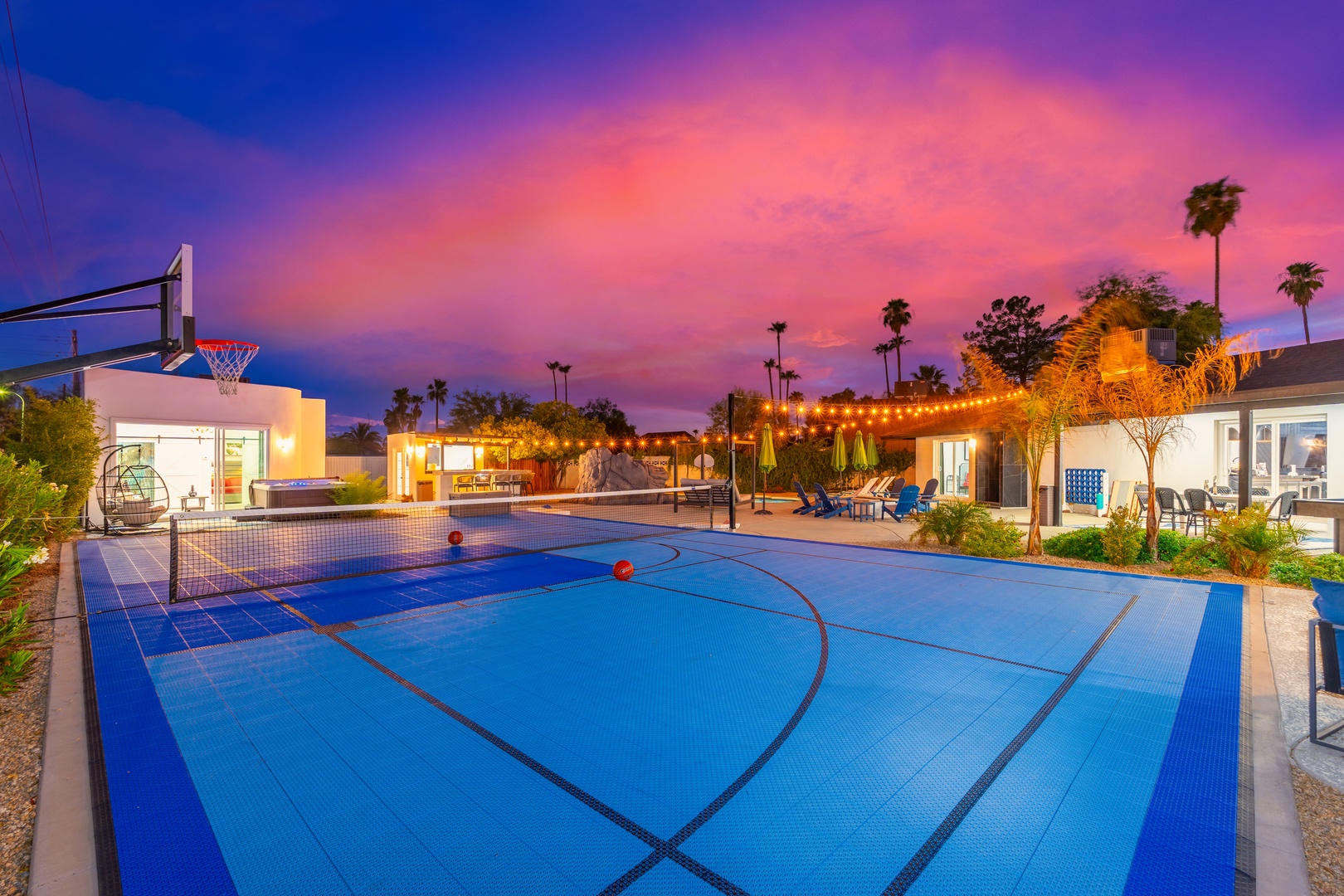 A stunning basketball court awaits under twilight skies, surrounded by palm trees, string lights, and spacious outdoor entertaining areas perfect for active getaways.