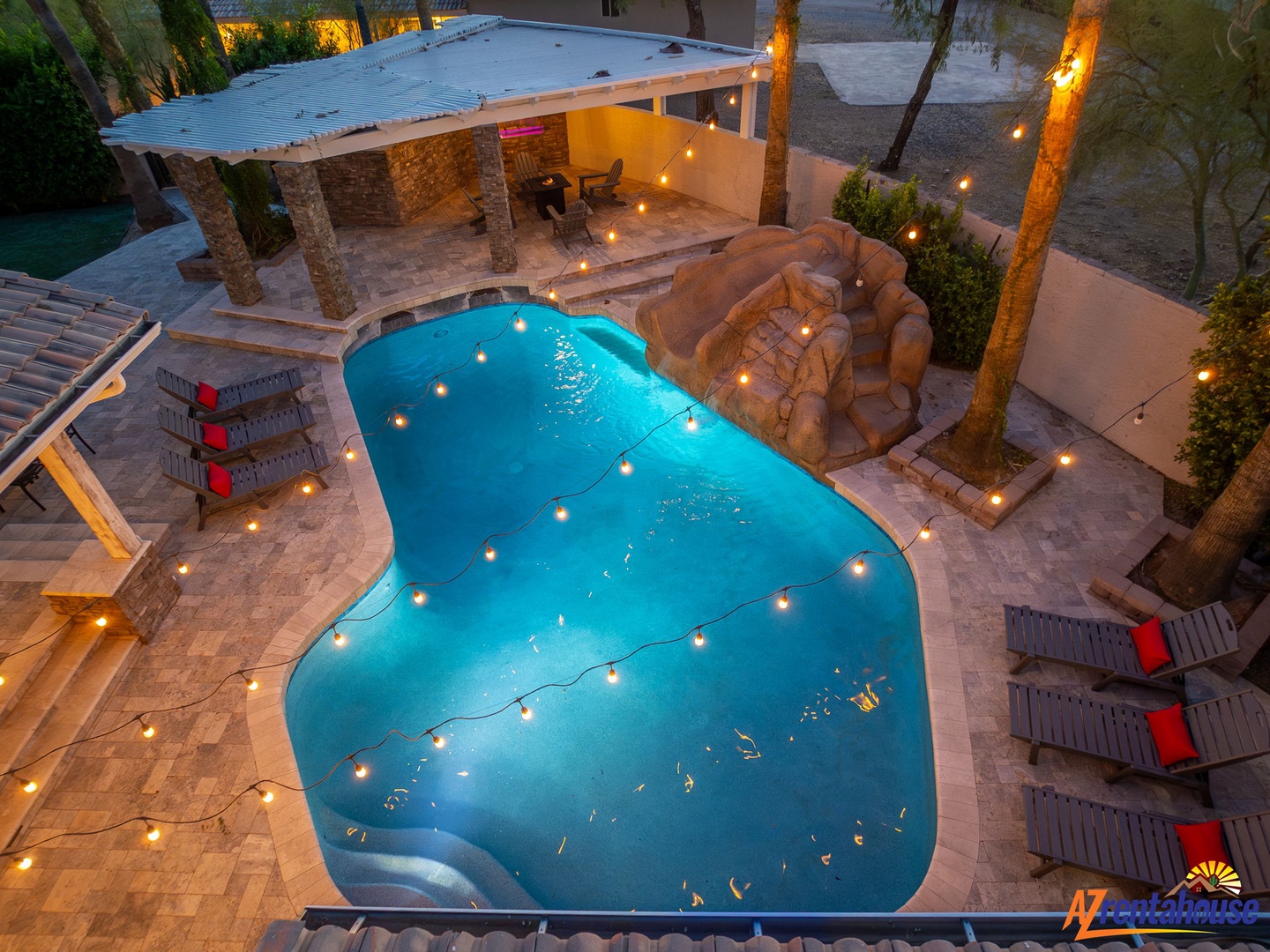 An aerial view captures the property's inviting pool area, complete with a covered patio and ambient lighting at dusk, offering a resort-style outdoor retreat.