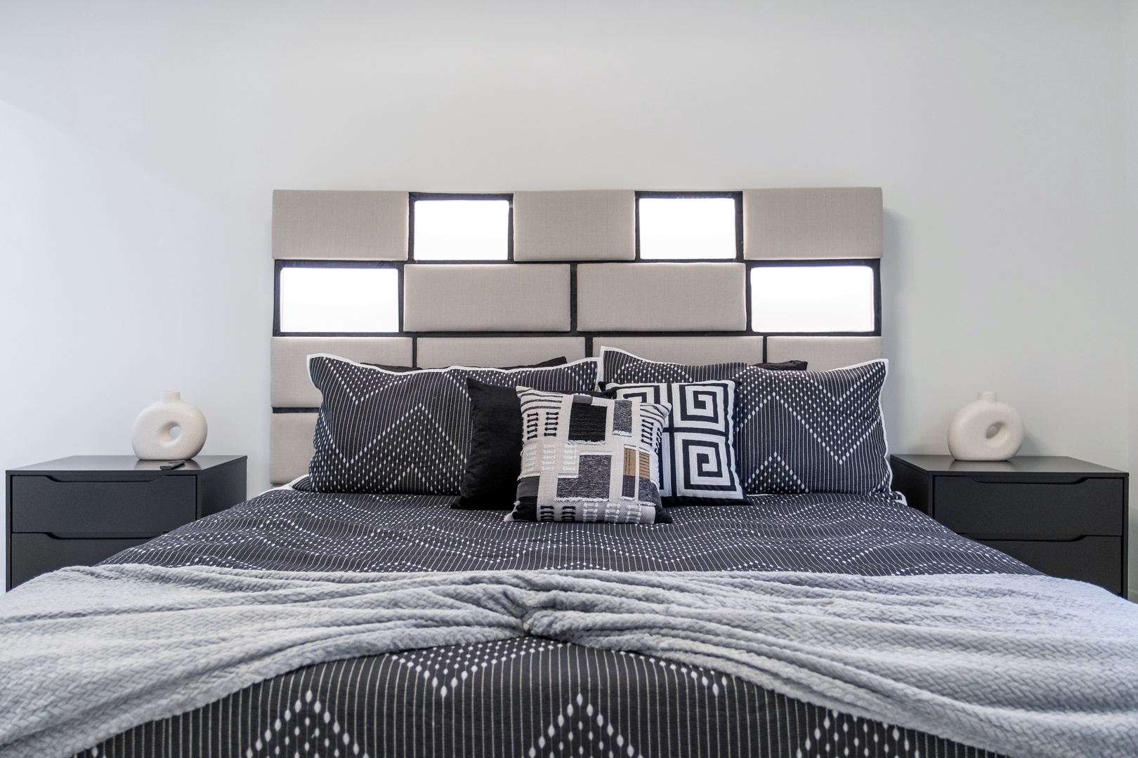 Sink into this plush bed with designer linens and a striking geometric headboard, flanked by sleek nightstands. Your peaceful retreat awaits in this modern, thoughtfully styled bedroom.