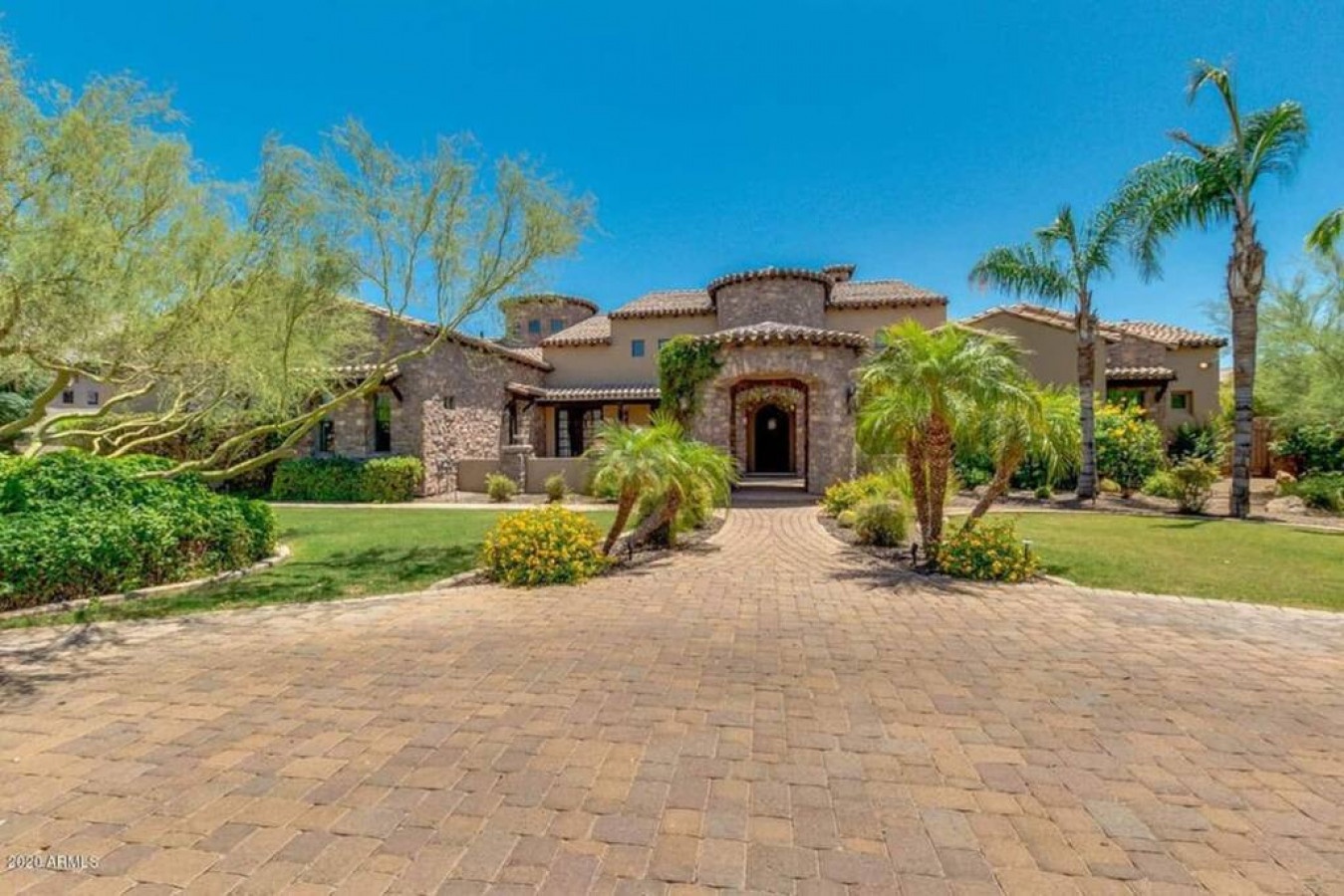 Mediterranean-style villa showcases elegant stone architecture surrounded by manicured desert landscaping and mature palm trees.