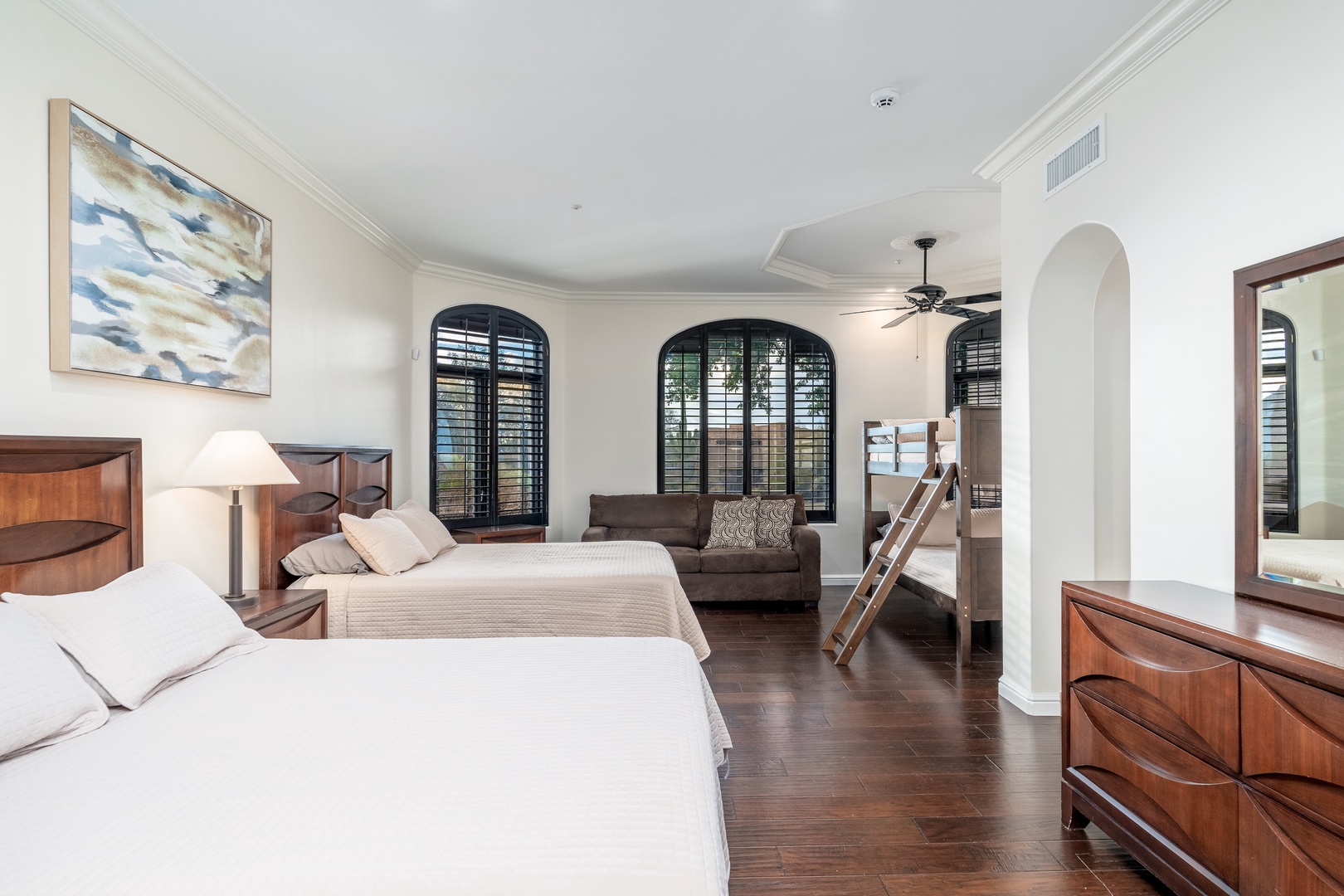Your spacious retreat features two plush beds, a cozy seating area, and elegant arched windows that invite natural light. Relax on dark hardwood floors surrounded by rich wood furnishings and coastal-inspired art.