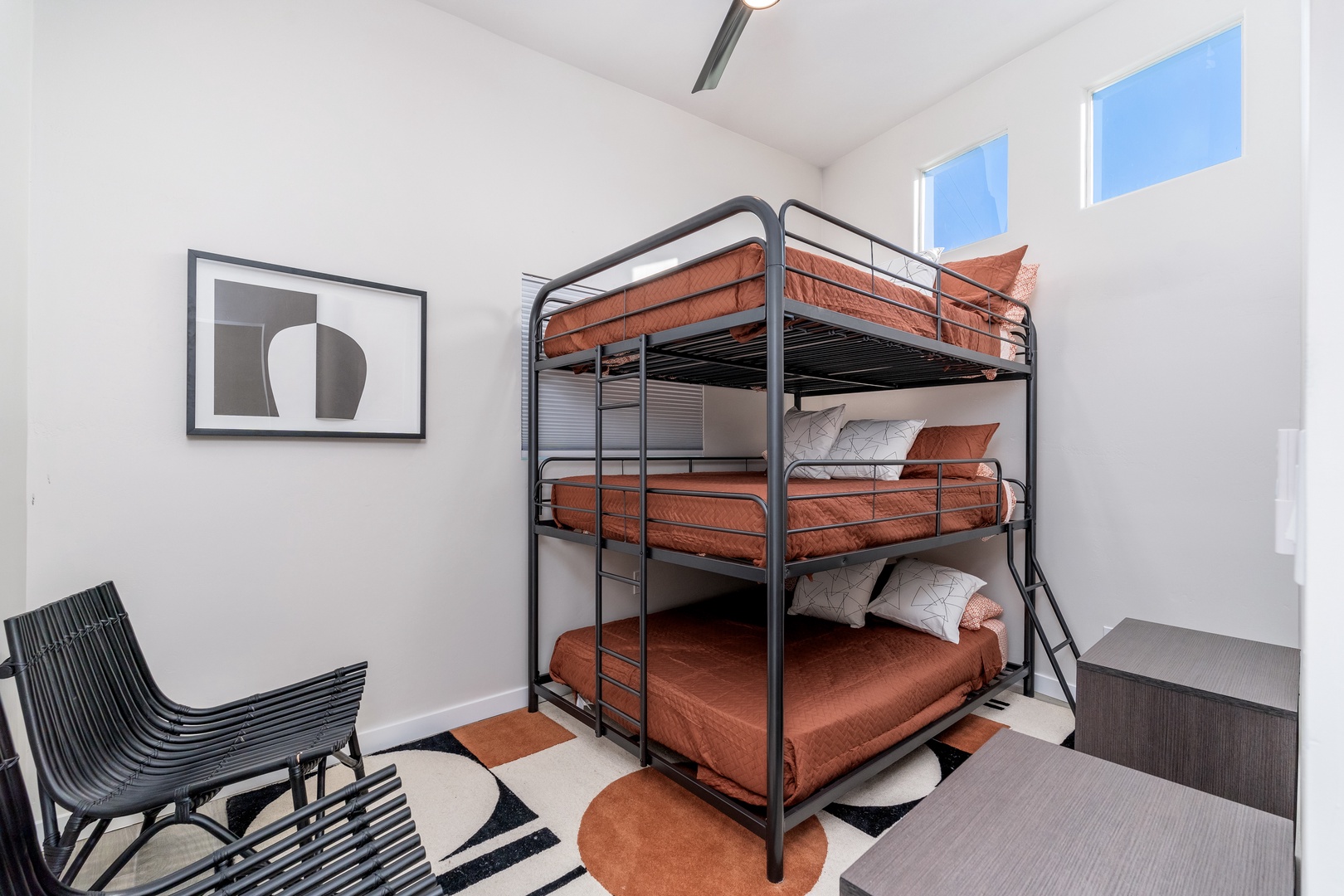 Sleep soundly in this bright bedroom designed for the whole family, featuring modern triple bunk beds dressed in warm rust-toned linens, minimalist décor, and sky-filled windows that bring in natural light.