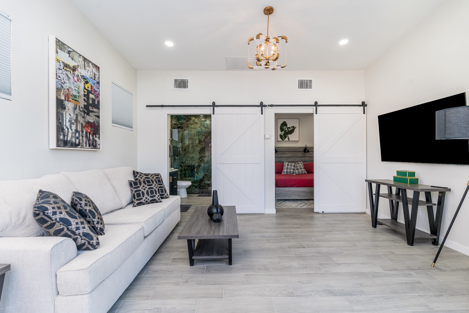 Relax in your bright living room with a cozy sofa, stylish barn doors leading to a bedroom, and a wall-mounted TV for your entertainment—your comfortable retreat awaits.