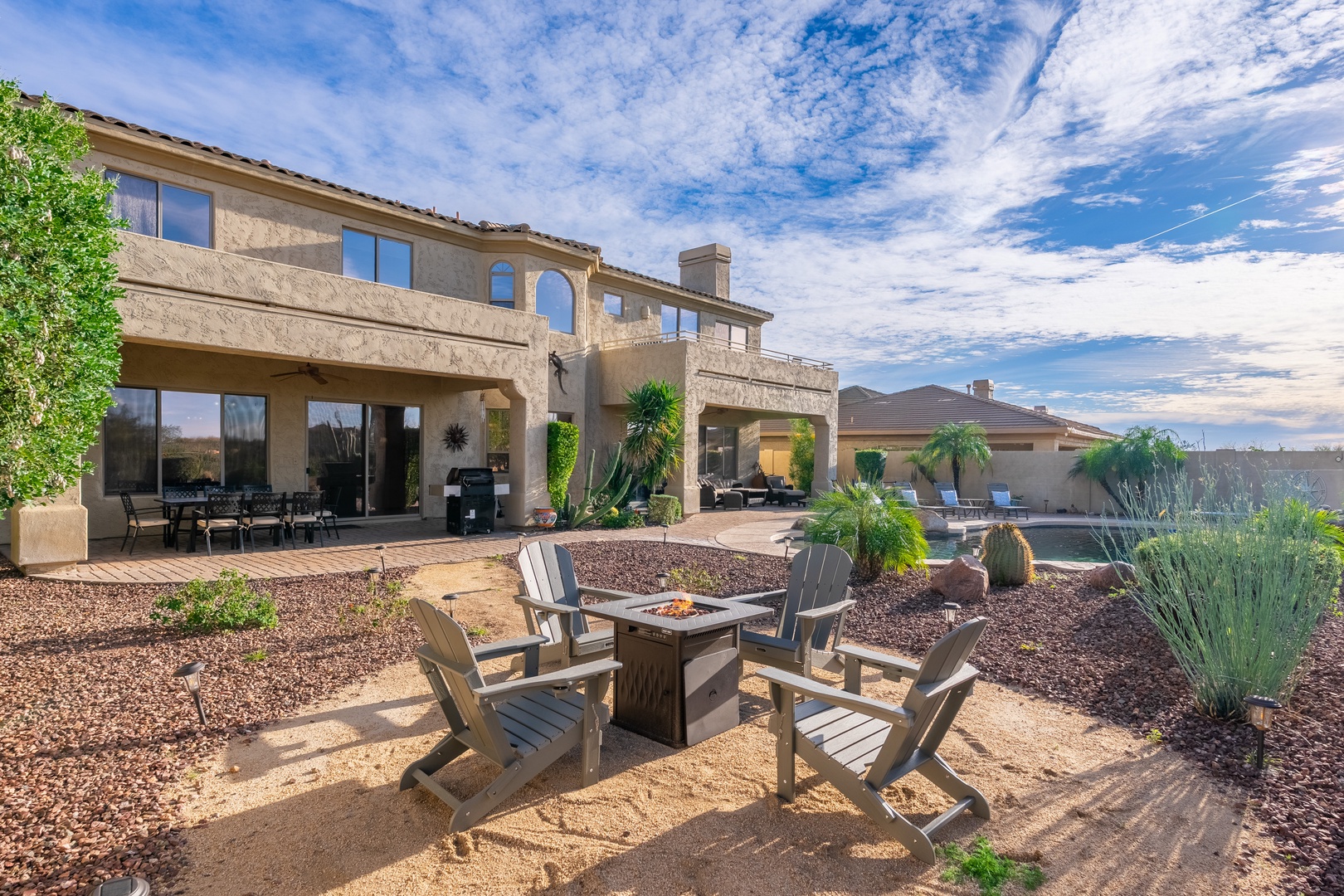 Spacious desert retreat featuring a charming fire pit with Adirondack seating, sparkling pool, and mountain-framed views under big Arizona skies.