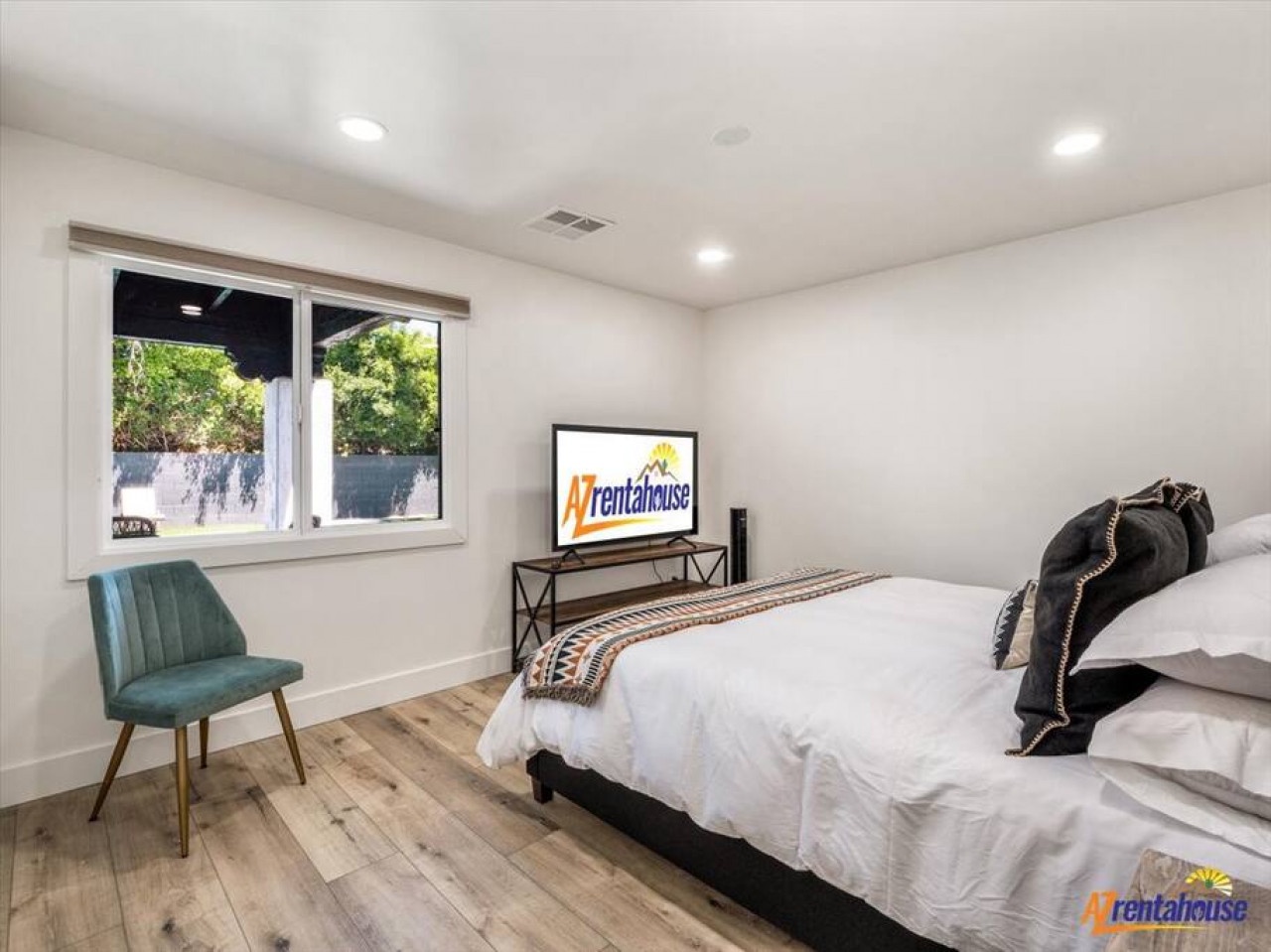 Rest peacefully in your bright bedroom featuring crisp white linens, modern TV entertainment, and garden views through the large window.