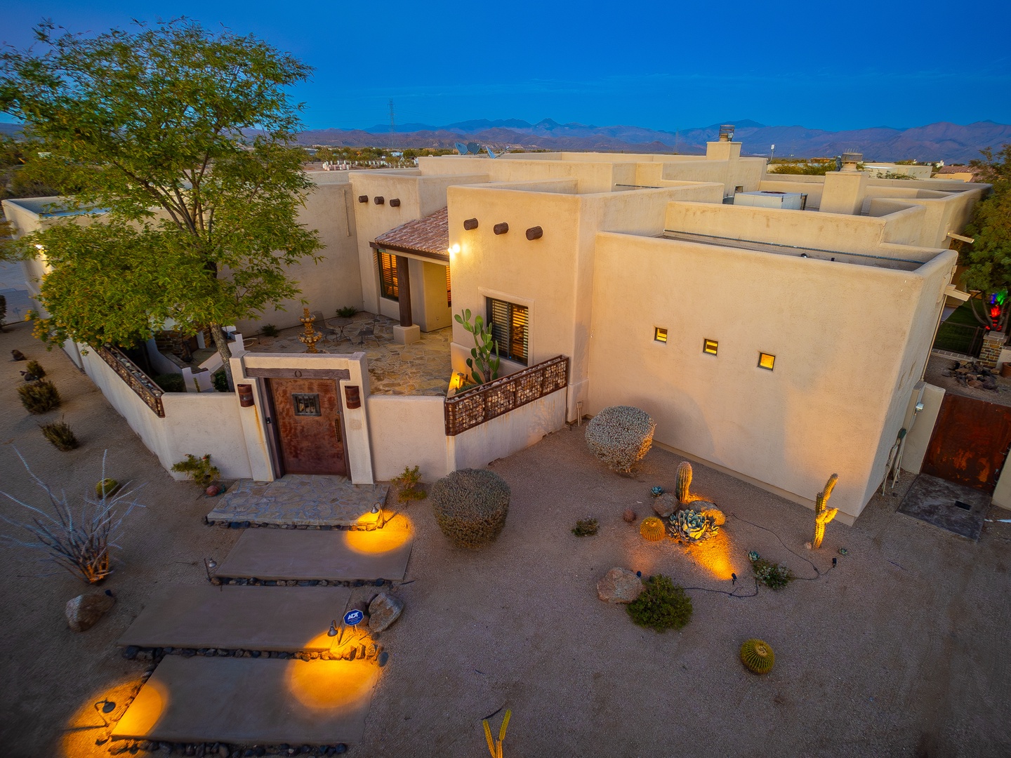 Southwestern-style property featuring adobe architecture, native desert landscaping with illuminated cacti and succulents, and distant mountain views under a clear blue sky.