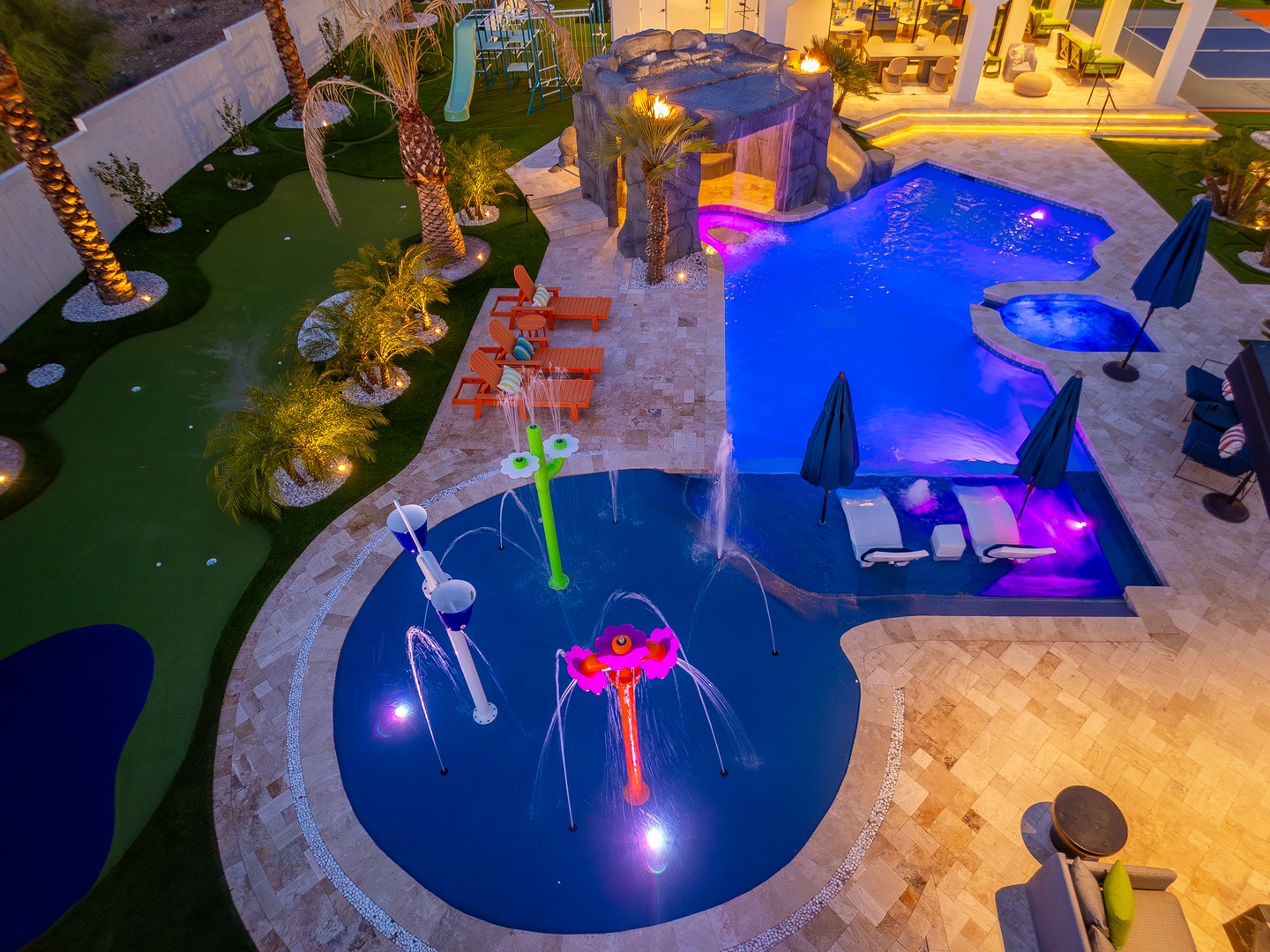 Aerial view showcases the resort's multi-level pool complex with vibrant lighting, splash features, putting greens, and tropical landscaping, creating an entertainment-focused outdoor space.