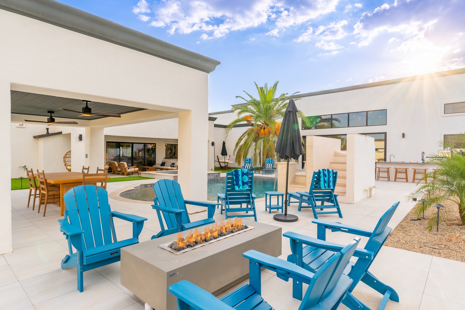 Gather around the modern fire pit with turquoise Adirondack chairs, where your private pool and covered outdoor dining await. Perfect for sunset gatherings under desert skies.