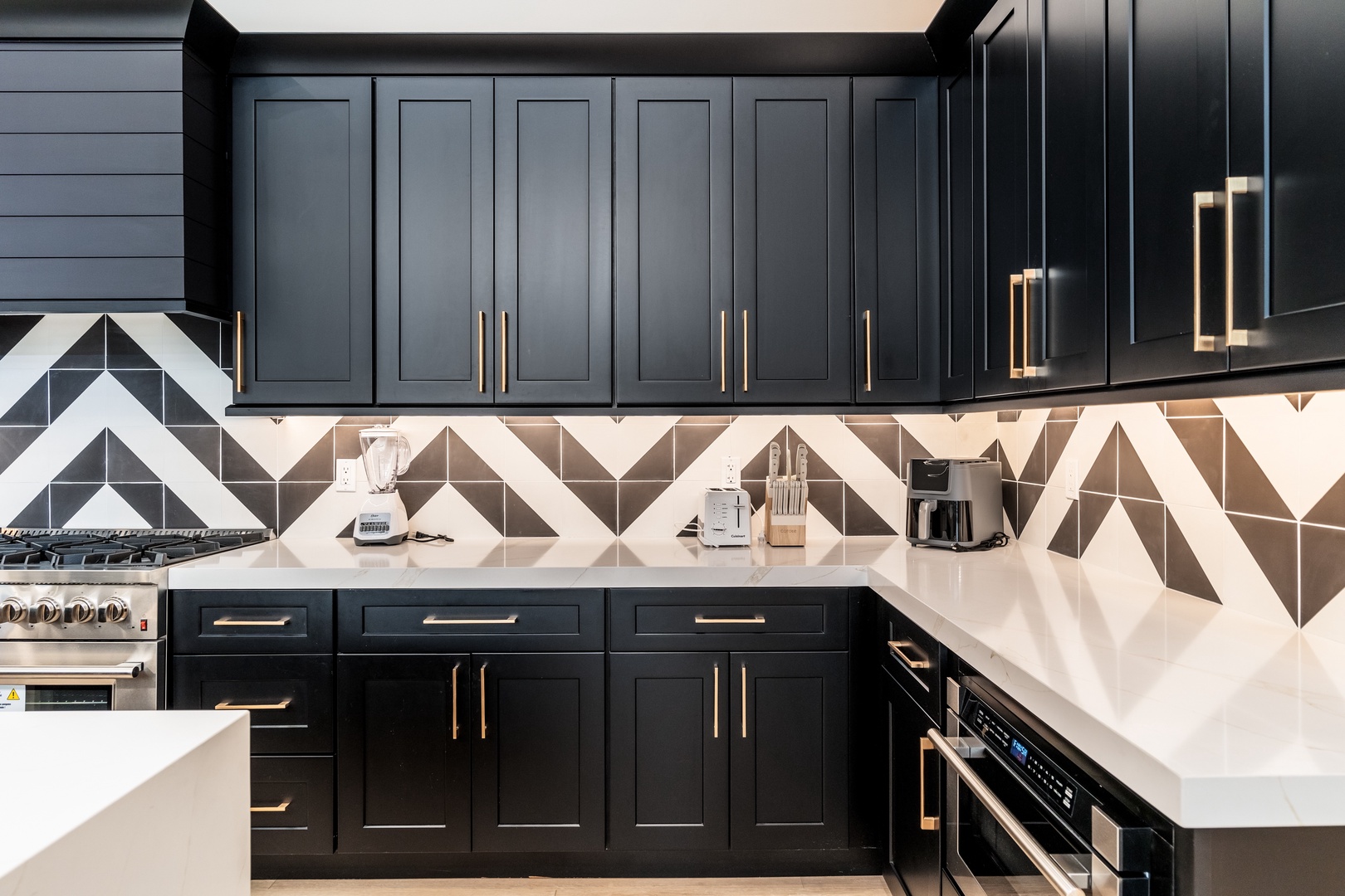 Your gourmet kitchen awaits with sleek black cabinetry, geometric tiled backsplash, modern appliances, and bright natural light from above—perfect for preparing memorable meals.