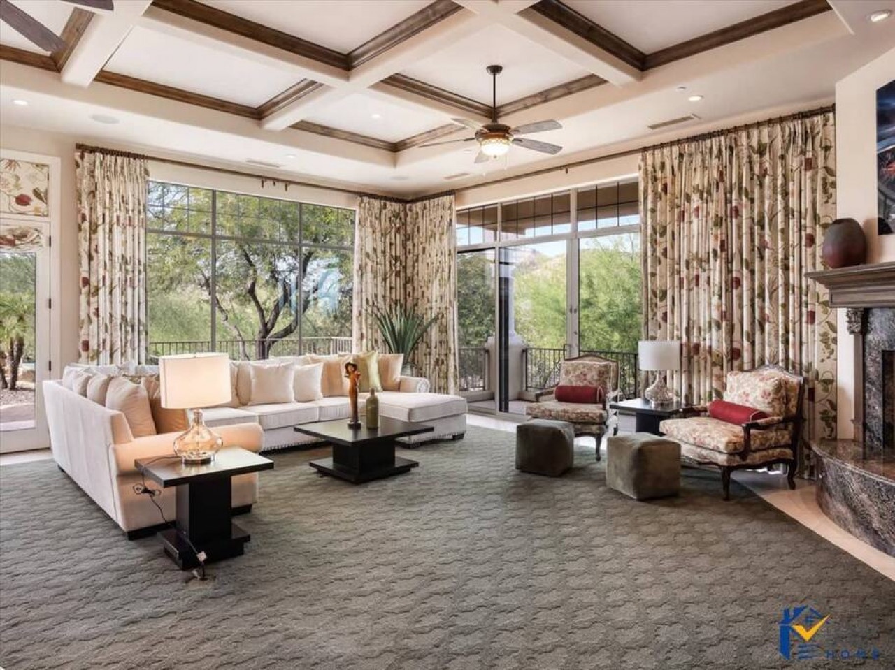 Relax in your elegant living room with coffered ceilings, cozy fireplace, and expansive windows showcasing beautiful garden views.