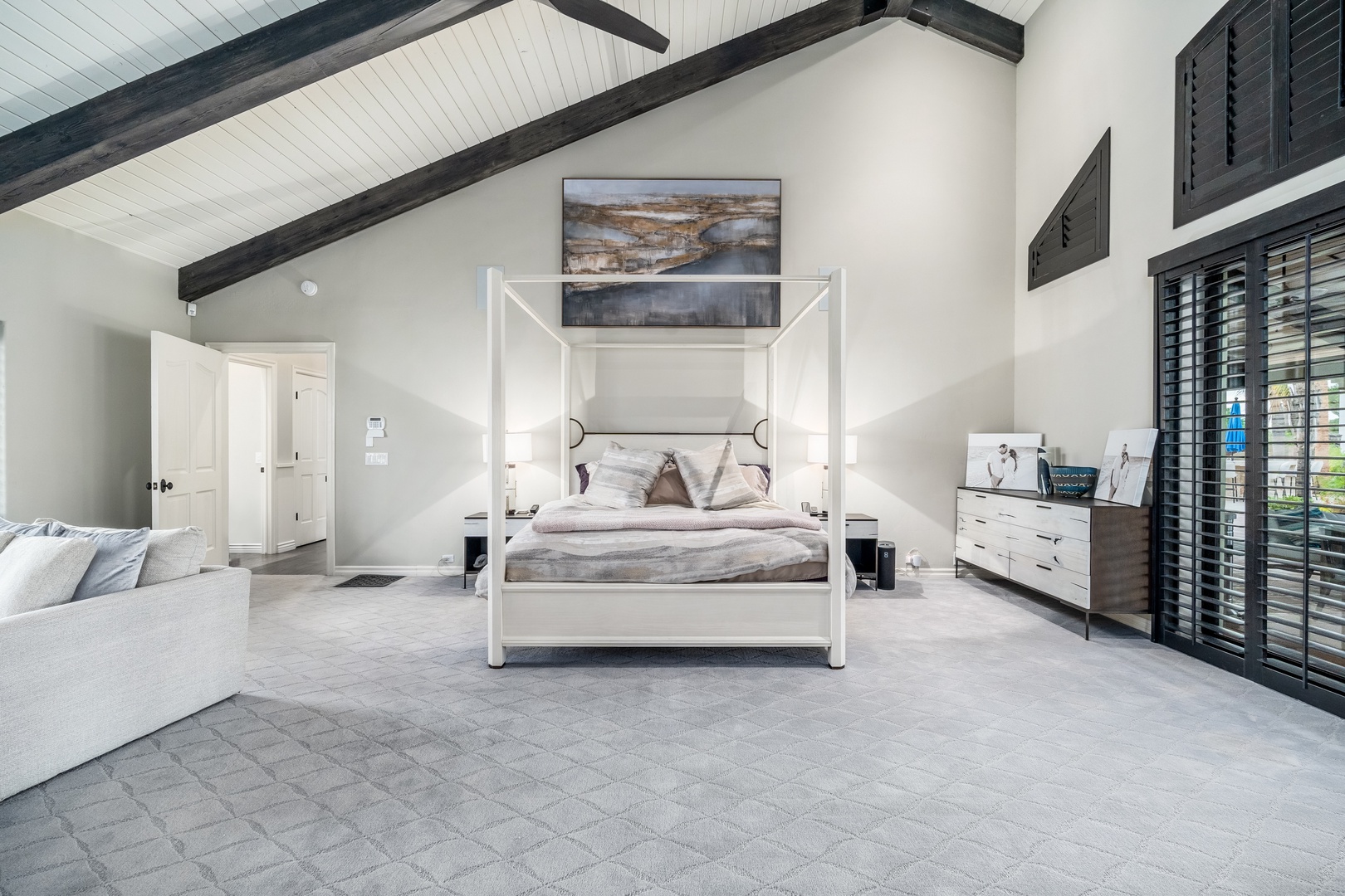 Drift into restful sleep beneath soaring beamed ceilings in your spacious master suite, where a striking four-poster bed and soft natural light create a serene, modern farmhouse retreat.