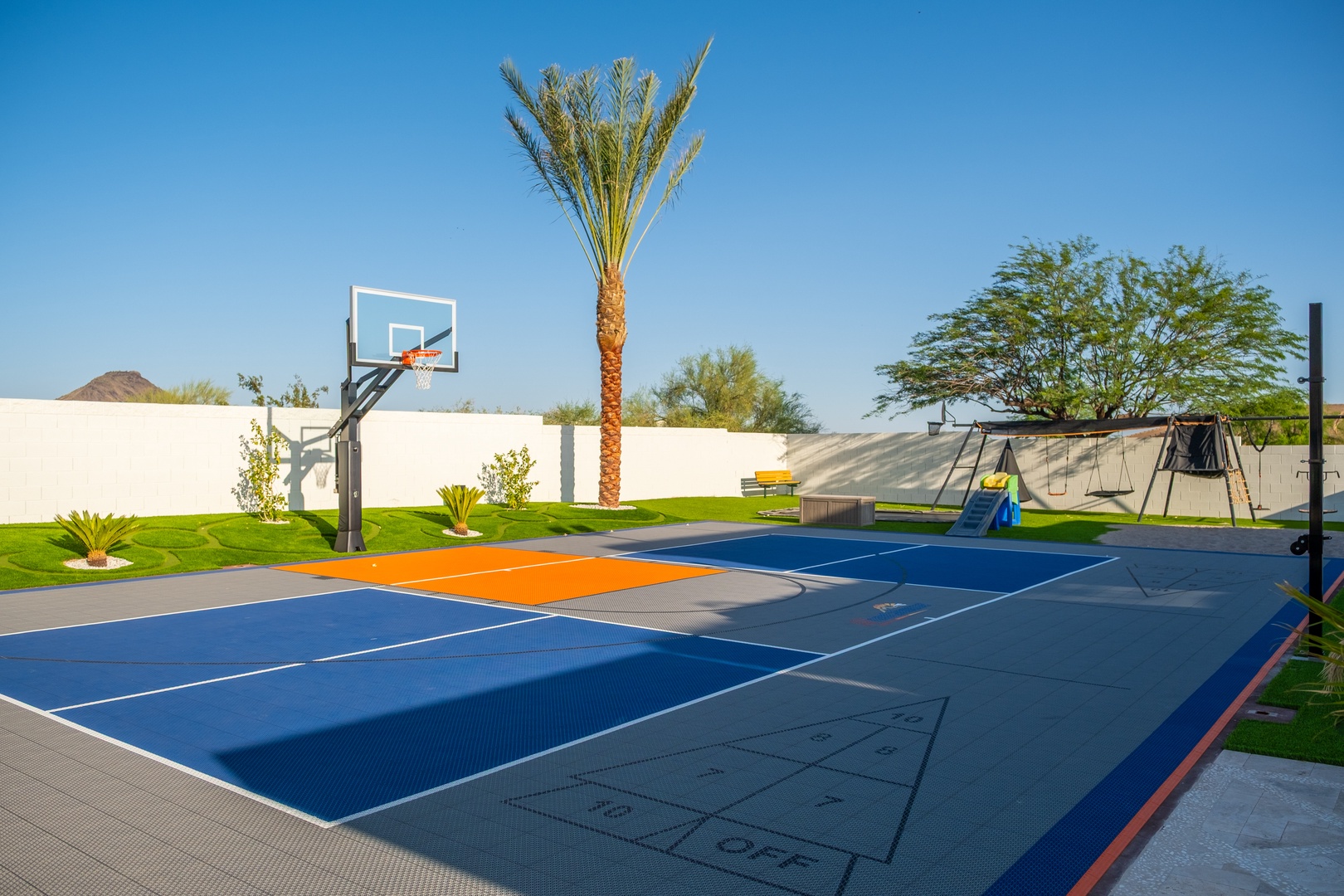 Private sport court and playground set against palm trees and sunny desert skies, perfect for family fun under clear blue horizons.