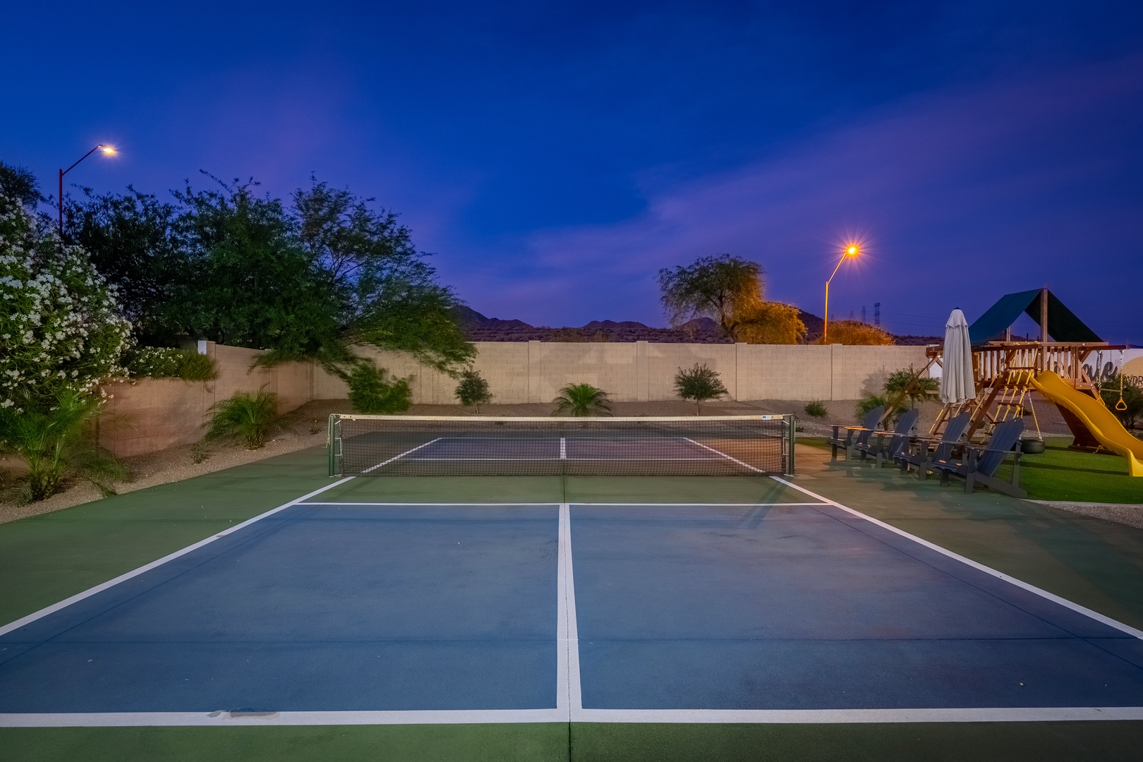 A private tennis court glows under twilight skies, offering endless fun for guests of all ages with a children's play area just steps away.