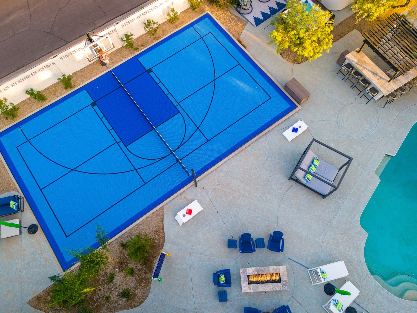 Aerial view showcasing the property's impressive recreational amenities including a full-size basketball court, sparkling pool, and modern outdoor lounge areas surrounded by landscaped greenery.
