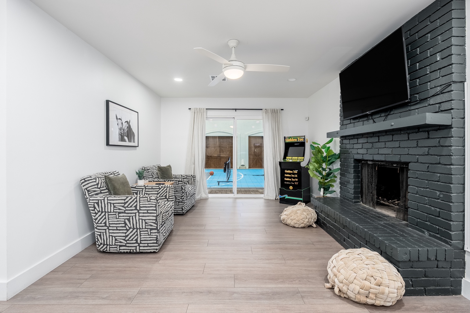 Unwind in your bright living room featuring stylish seating, a cozy fireplace, and direct pool access. A chic ceiling fan and modern finishes make it your perfect retreat.