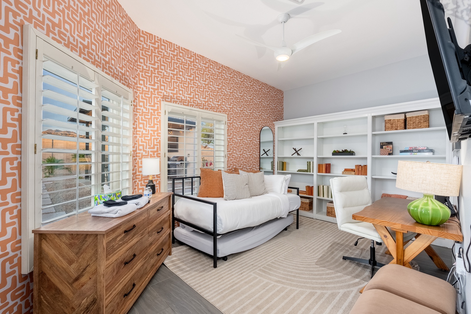 Relax in your sunlit bedroom featuring custom built-in shelving, a cozy daybed, and vibrant geometric wallpaper that adds personality to your space.