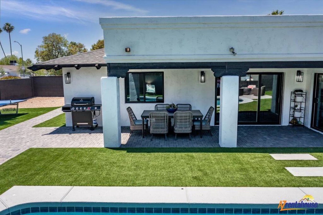Modern property with covered patio dining area and BBQ grill overlooking pristine lawn and pool deck.