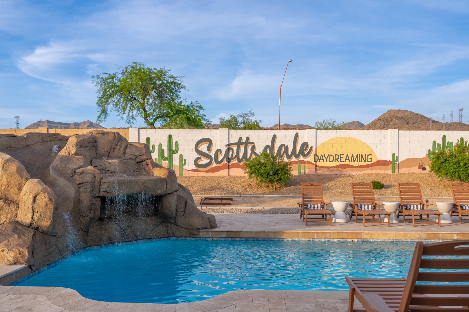 A desert oasis pool with cascading waterfall, loungers, and mountain views under bright Arizona skies—located near the Scottsdale community entrance marker.