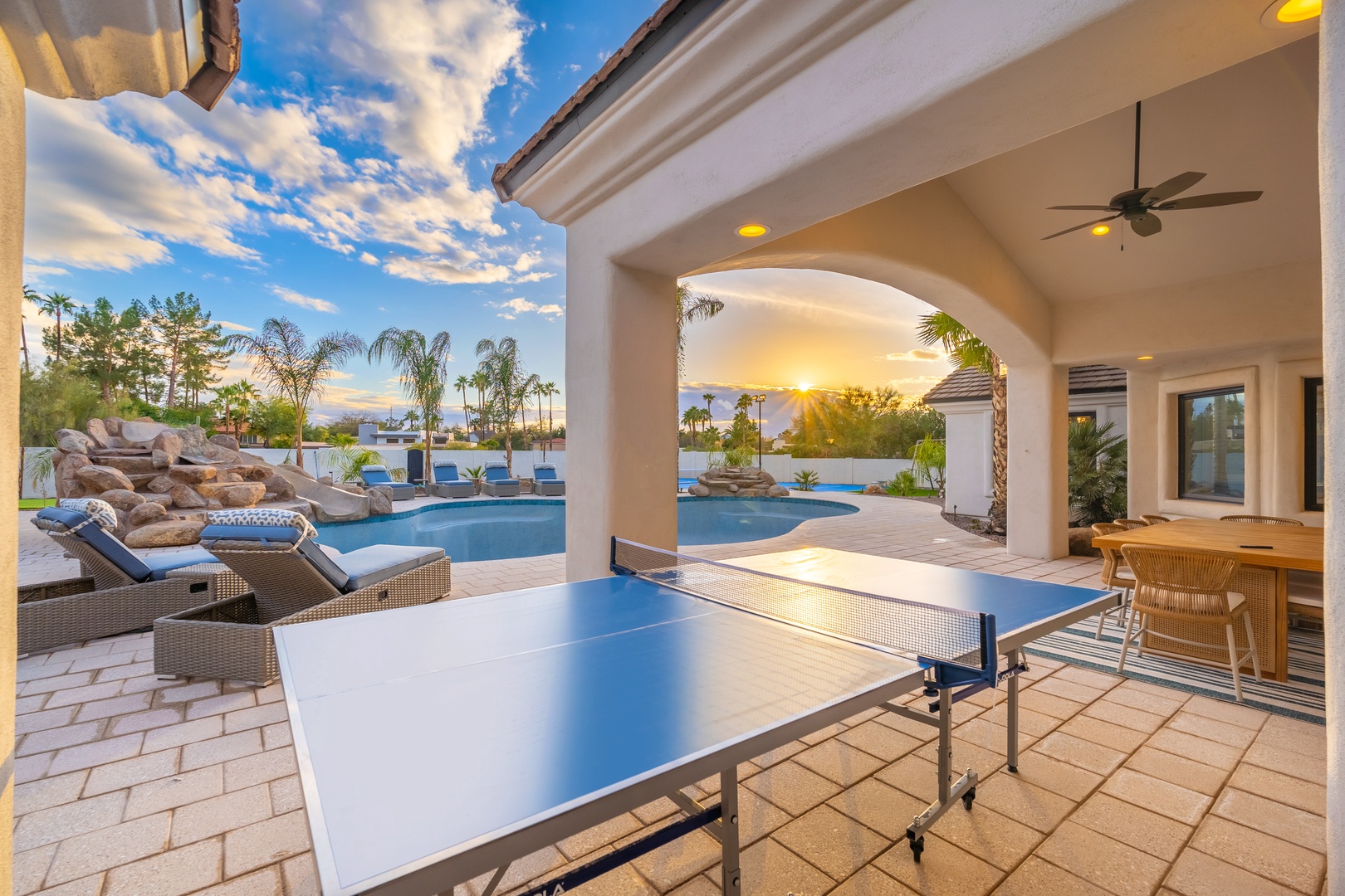 Step onto your covered patio where table tennis awaits, framing a stunning pool, waterfall feature, and golden sunset views that promise unforgettable evenings of relaxation and fun.
