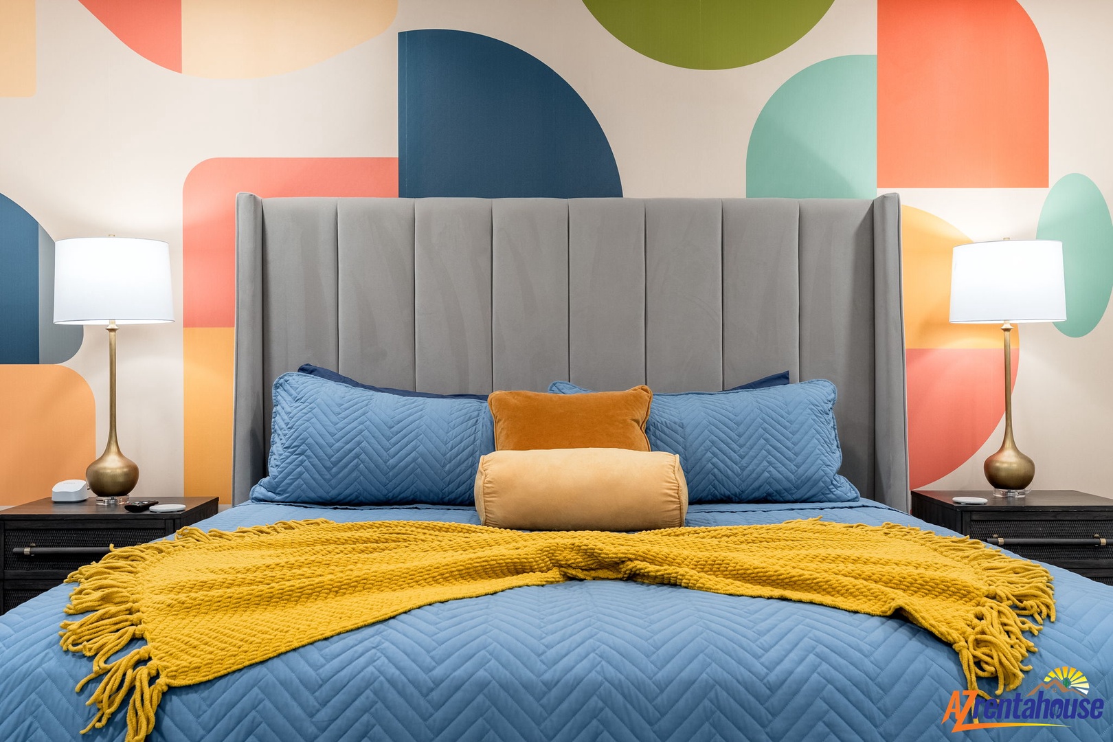 Sink into your stylish bedroom featuring a plush upholstered headboard, vibrant geometric wallpaper, and cozy golden accents for a perfect night's rest.