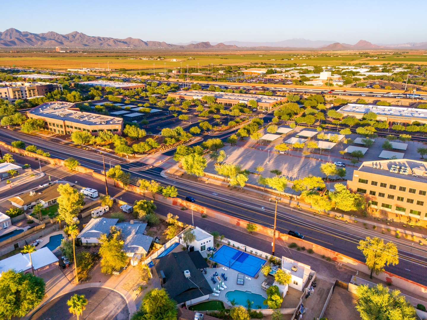 Aerial view of the property nestled in a vibrant desert community, with mountain ranges framing the horizon and lush greenery dotting the surrounding neighborhood.