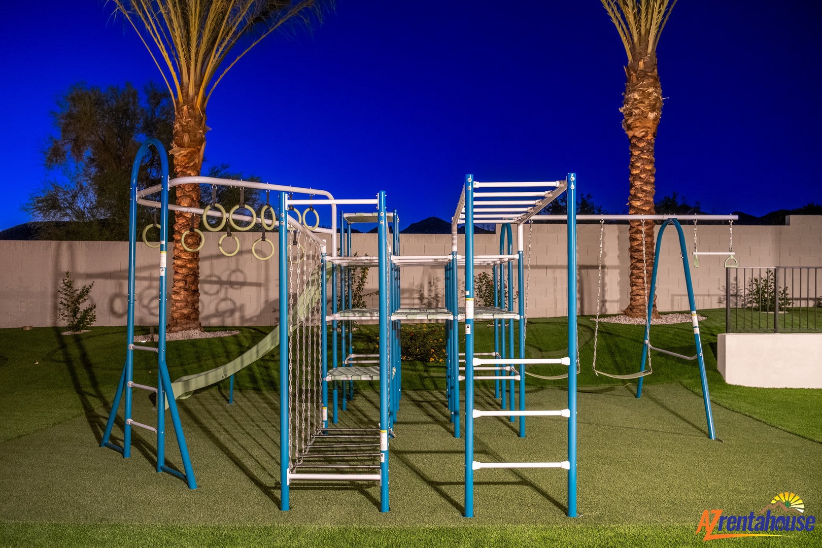 Modern playground with climbing structures and swings set among palm trees and manicured lawns at twilight.