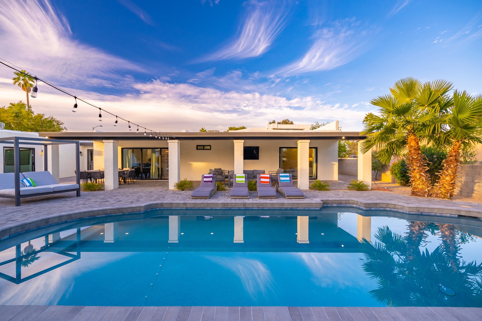 Modern desert oasis with a sparkling pool, colorful loungers, and palm trees under a dramatic sky—your perfect poolside retreat awaits.