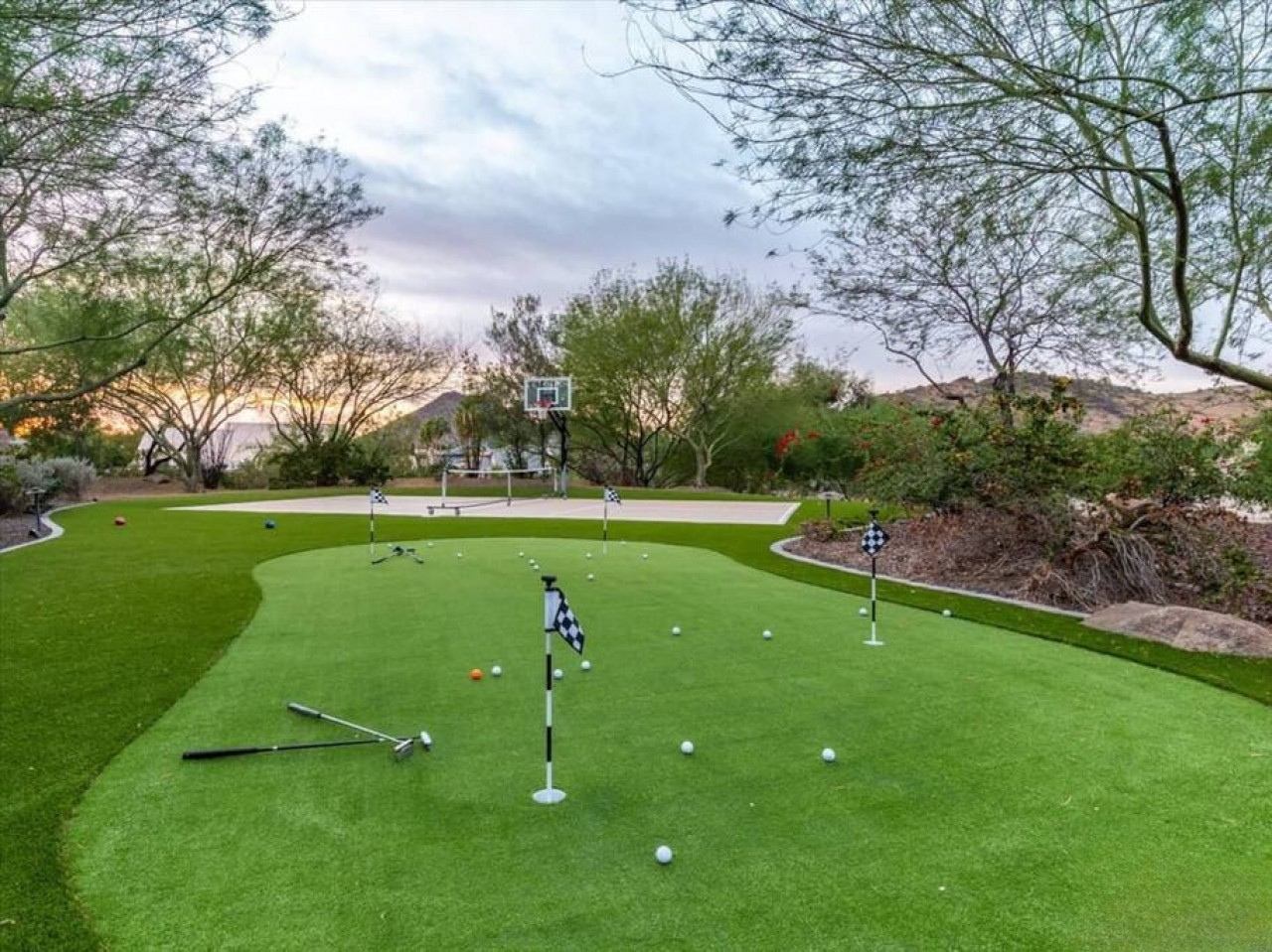 A private putting green set within lush landscaping, featuring multiple holes and a basketball hoop, creating an ideal space for outdoor recreation and practice.
